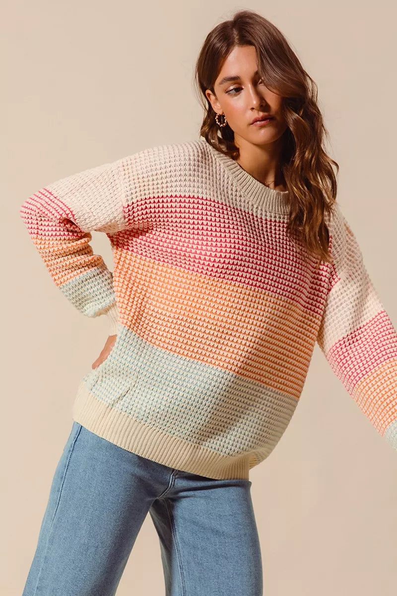 Woman wearing a pastel color block waffle-knit sweater in pink, orange, and blue tones — cozy ribbed pullover from A Whimsical Affair.