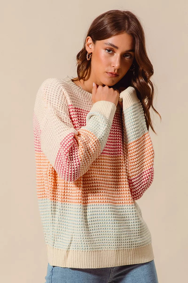Woman wearing a pastel color block waffle-knit sweater in pink, orange, and blue tones — cozy ribbed pullover from A Whimsical Affair.