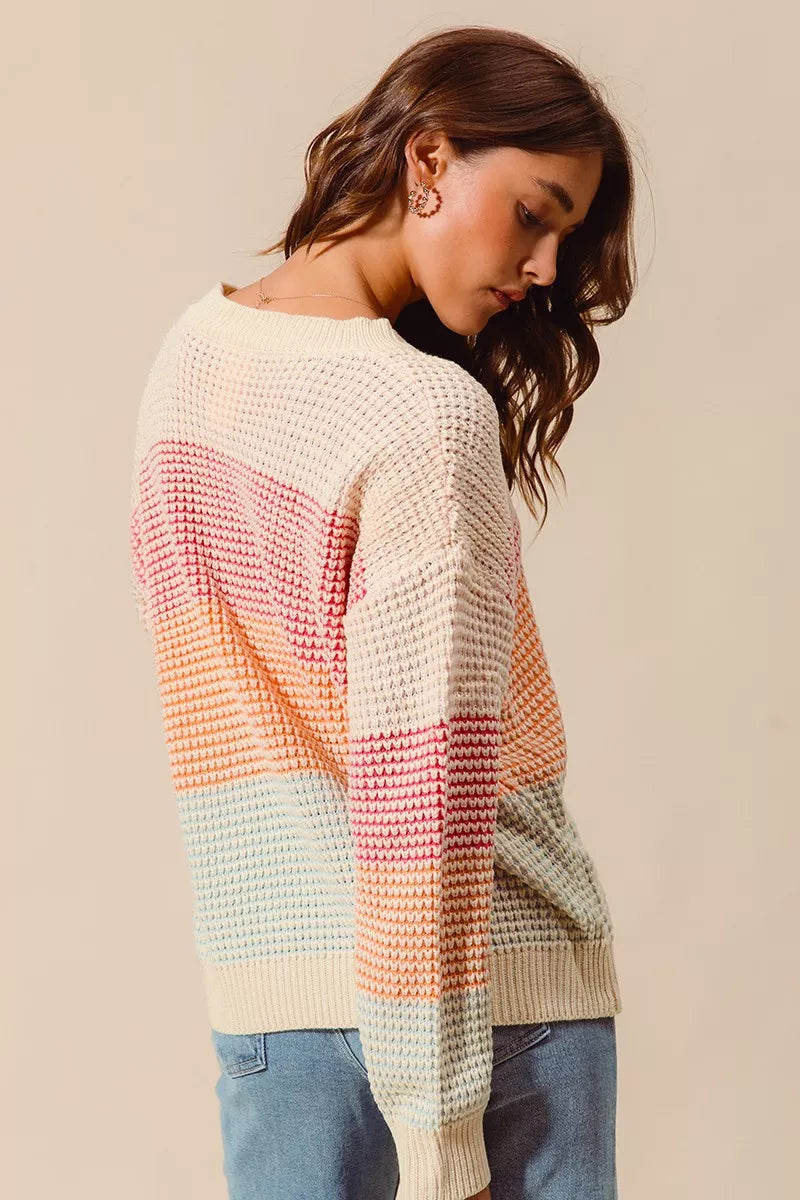 Woman wearing a pastel color block waffle-knit sweater in pink, orange, and blue tones — cozy ribbed pullover from A Whimsical Affair.