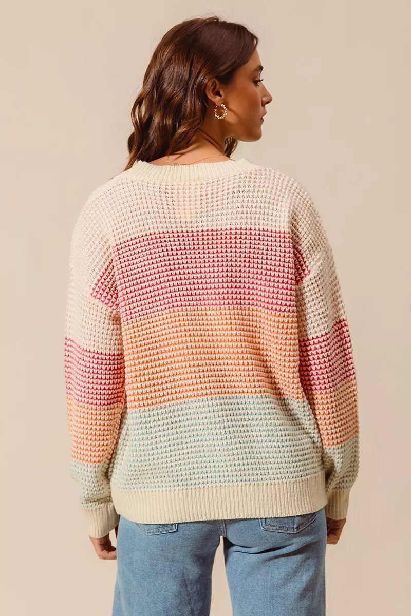 Woman wearing a pastel color block waffle-knit sweater in pink, orange, and blue tones — cozy ribbed pullover from A Whimsical Affair.