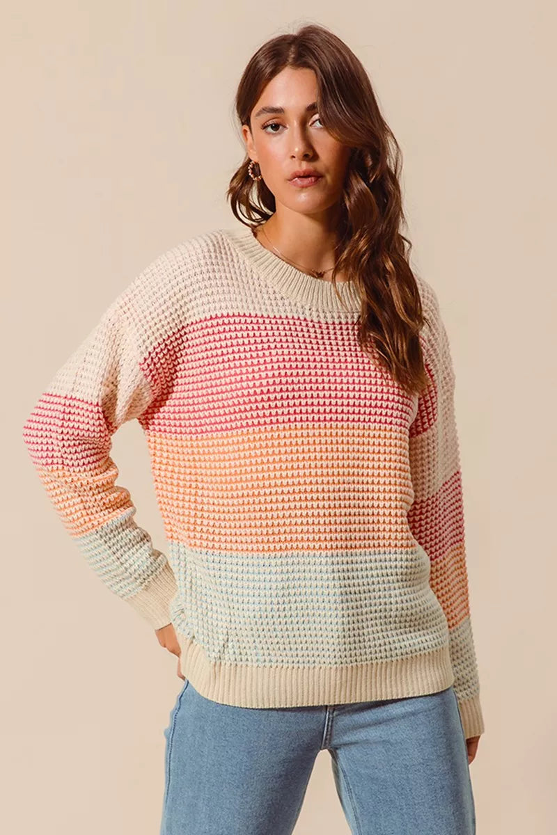 Woman wearing a pastel color block waffle-knit sweater in pink, orange, and blue tones — cozy ribbed pullover from A Whimsical Affair.
