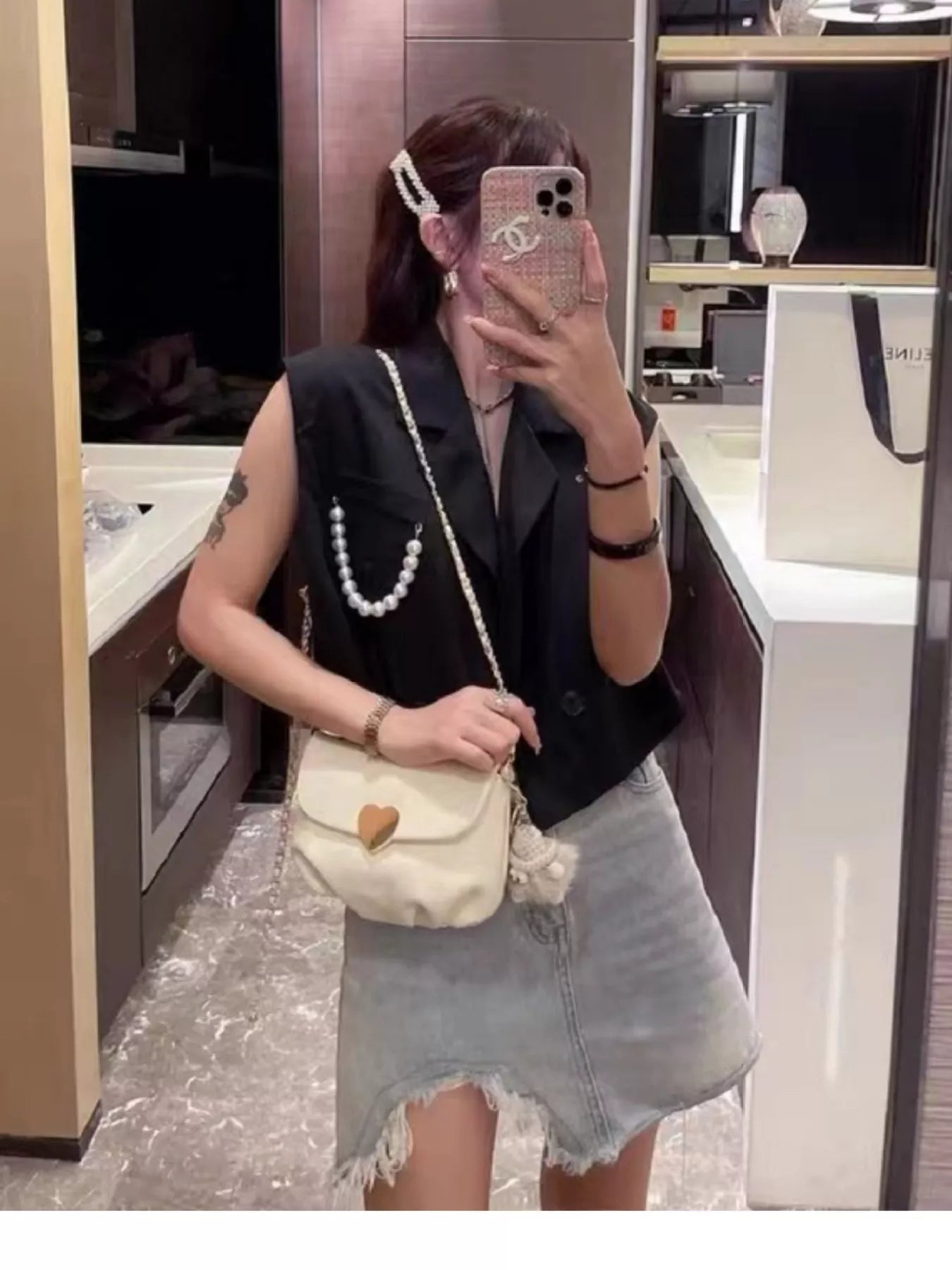 Cream mini crossbody bag with gold heart clasp and chain strap resting on beige fabric.