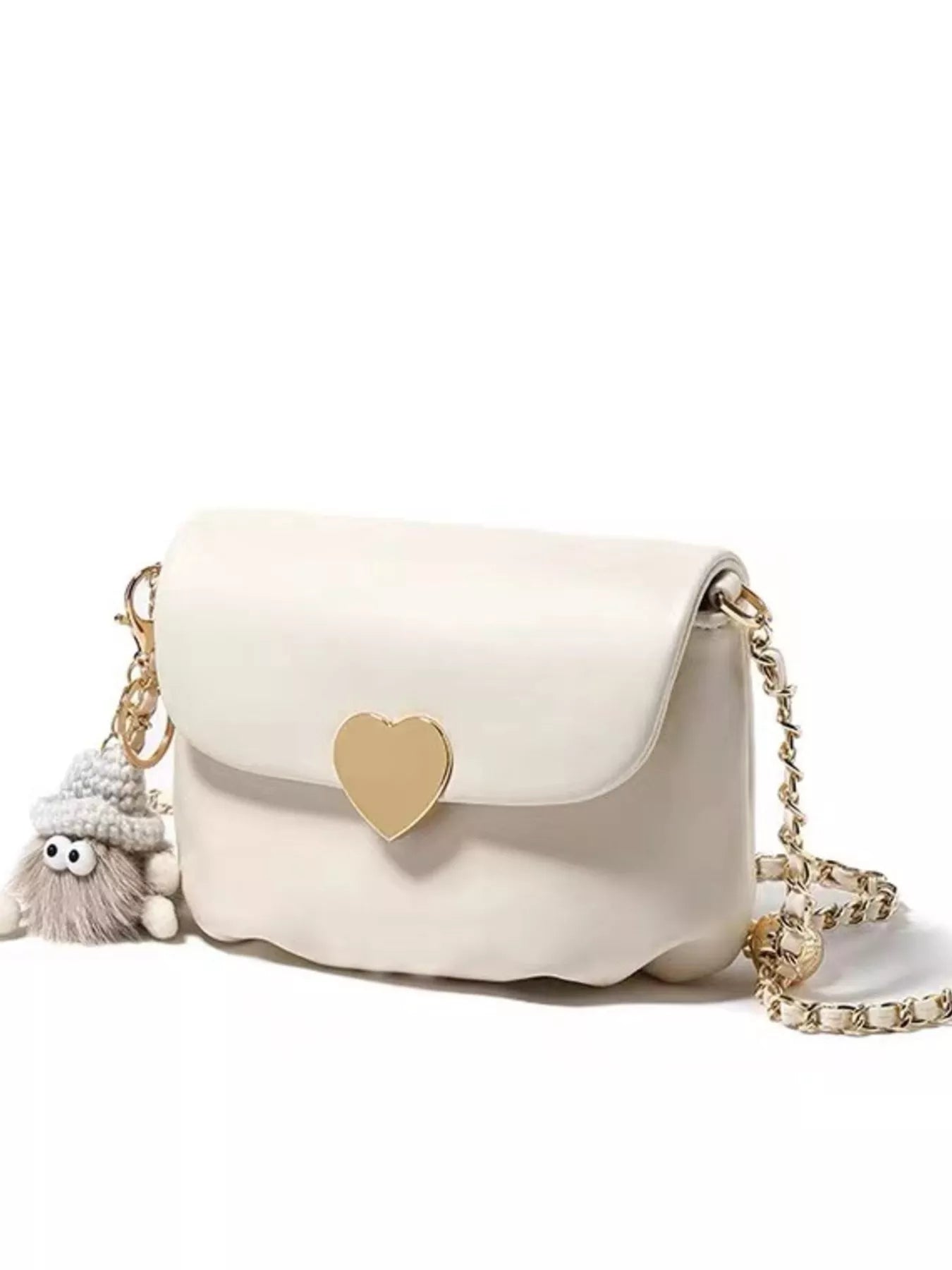 Cream mini crossbody bag with gold heart clasp and chain strap resting on beige fabric.