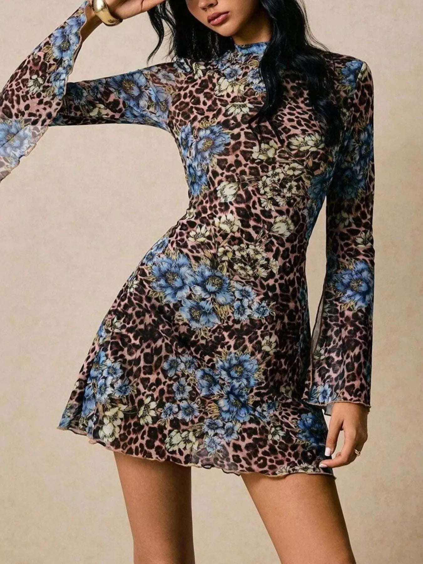 Model wearing a long-sleeve mesh mini dress featuring a mixed leopard and blue floral print with slit sleeves and a fitted silhouette.