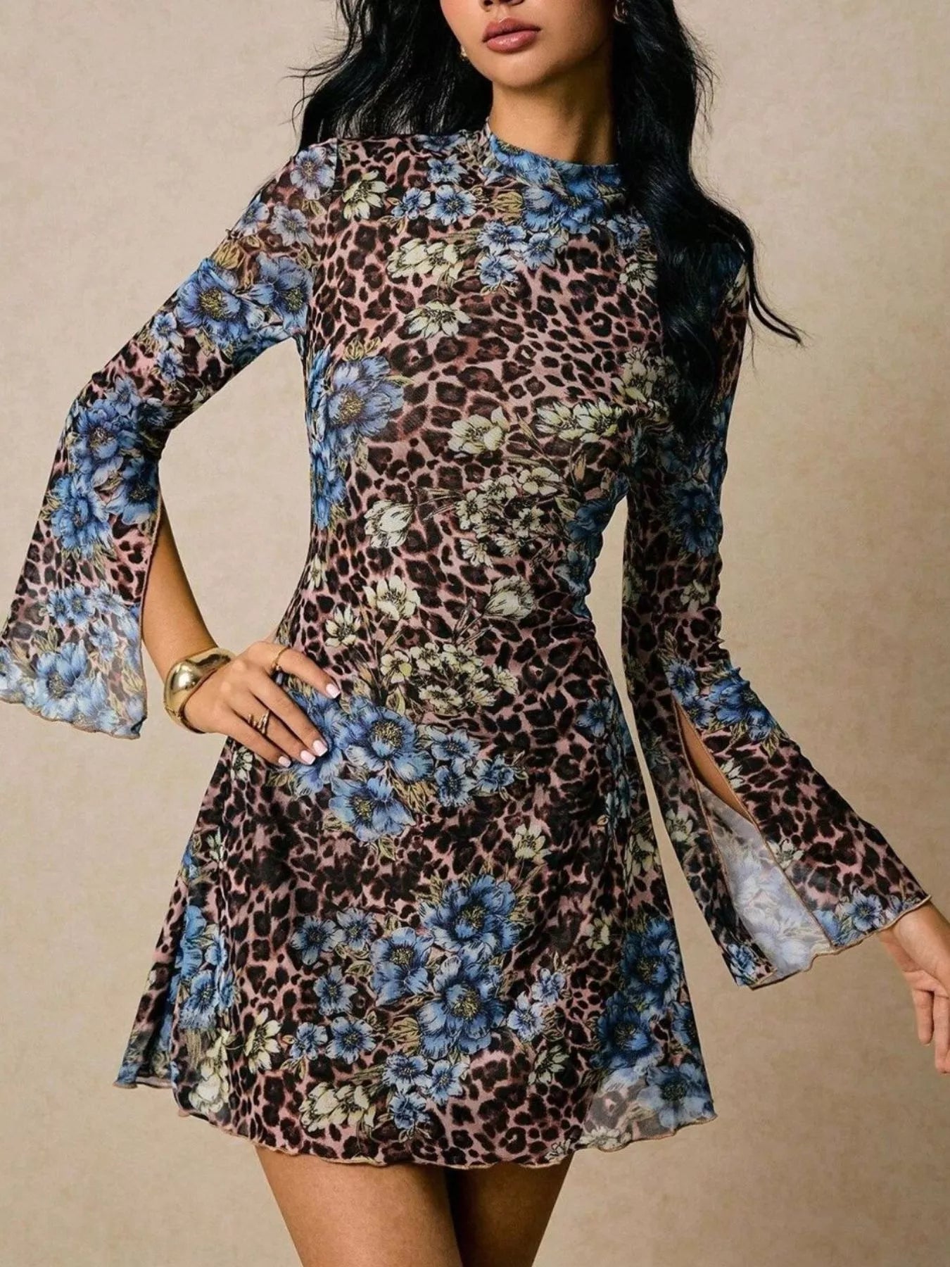 Model wearing a long-sleeve mesh mini dress featuring a mixed leopard and blue floral print with slit sleeves and a fitted silhouette.
