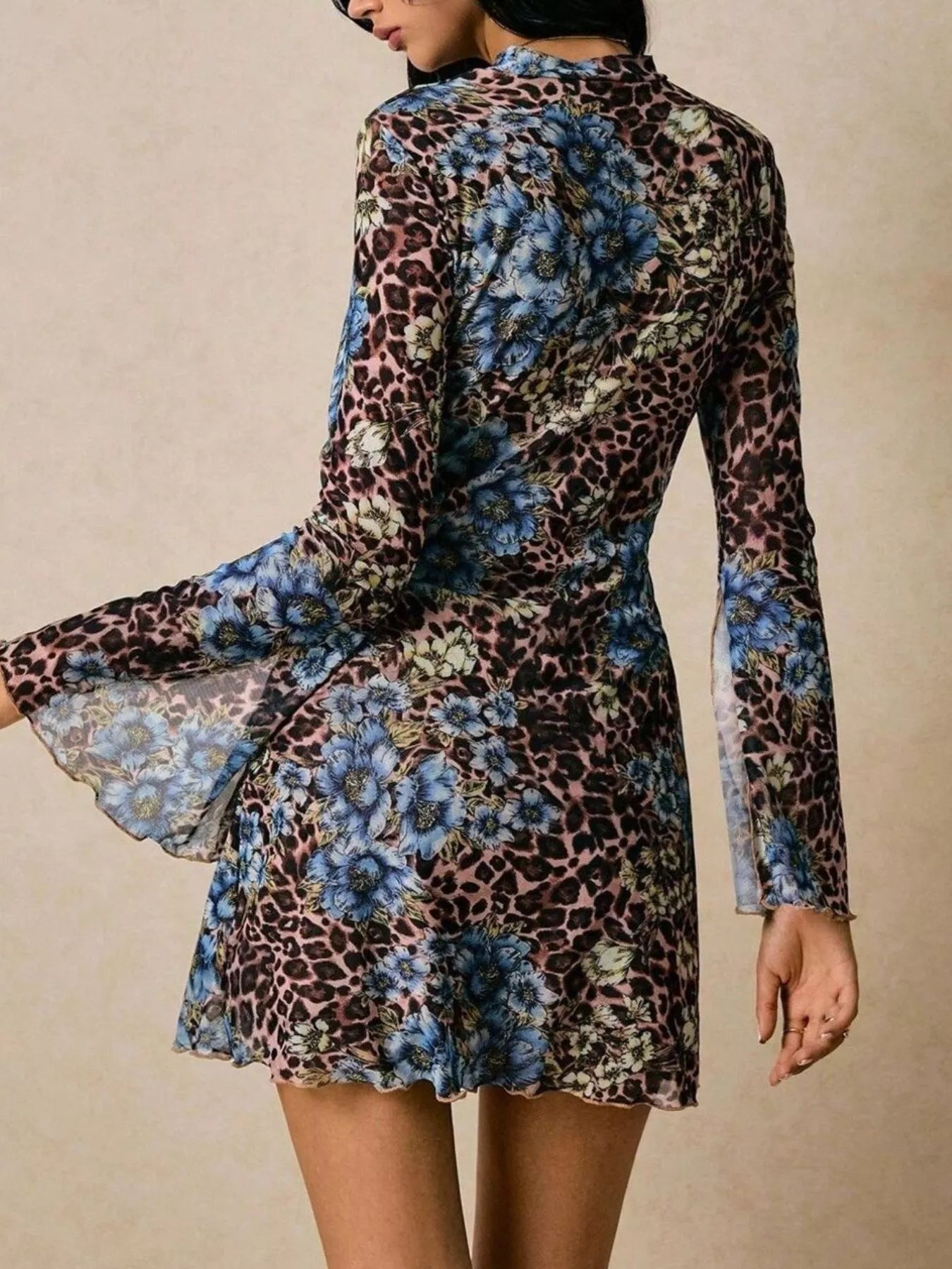 Model wearing a long-sleeve mesh mini dress featuring a mixed leopard and blue floral print with slit sleeves and a fitted silhouette.