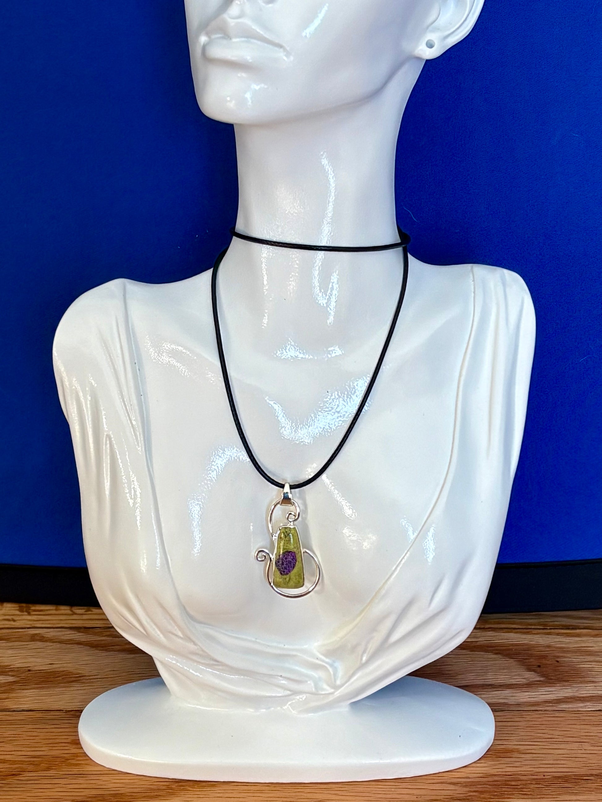 Green Alantiste crystal pendant with natural purple inclusion wrapped in silver wire on wooden surface