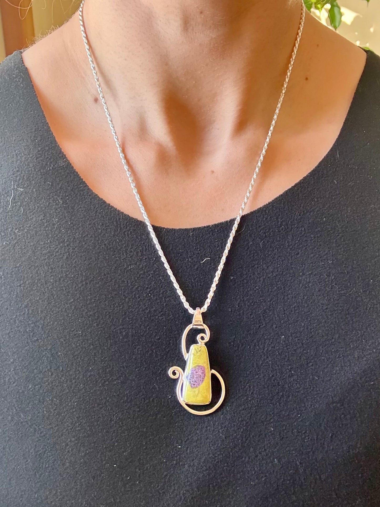 Green Alantiste crystal pendant with natural purple inclusion wrapped in silver wire on wooden surface