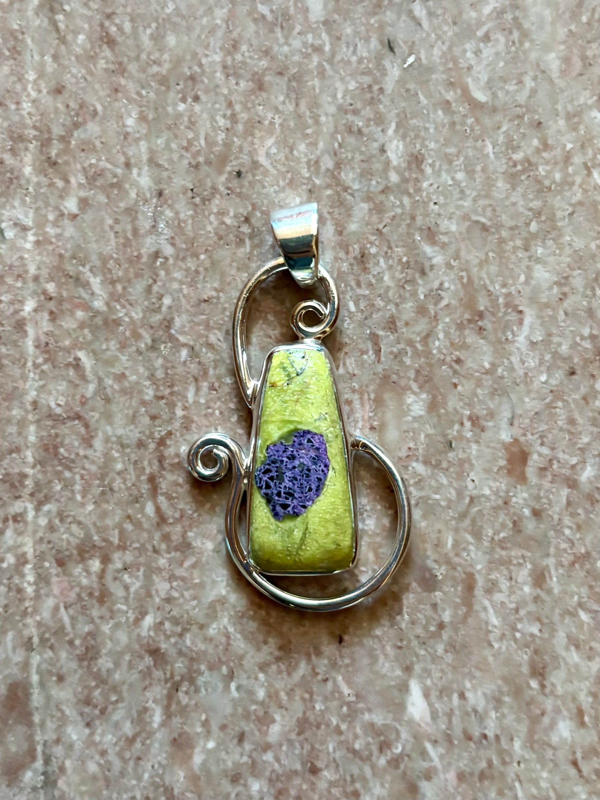 Green Alantiste crystal pendant with natural purple inclusion wrapped in silver wire on wooden surface