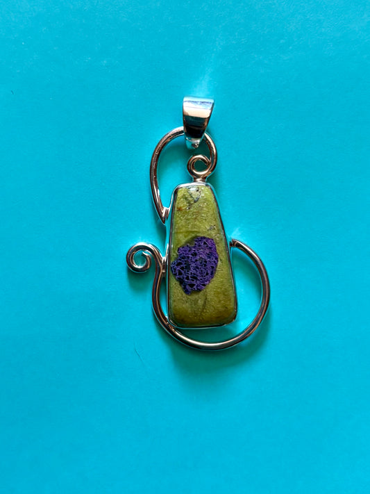 Green Alantiste crystal pendant with natural purple inclusion wrapped in silver wire on wooden surface
