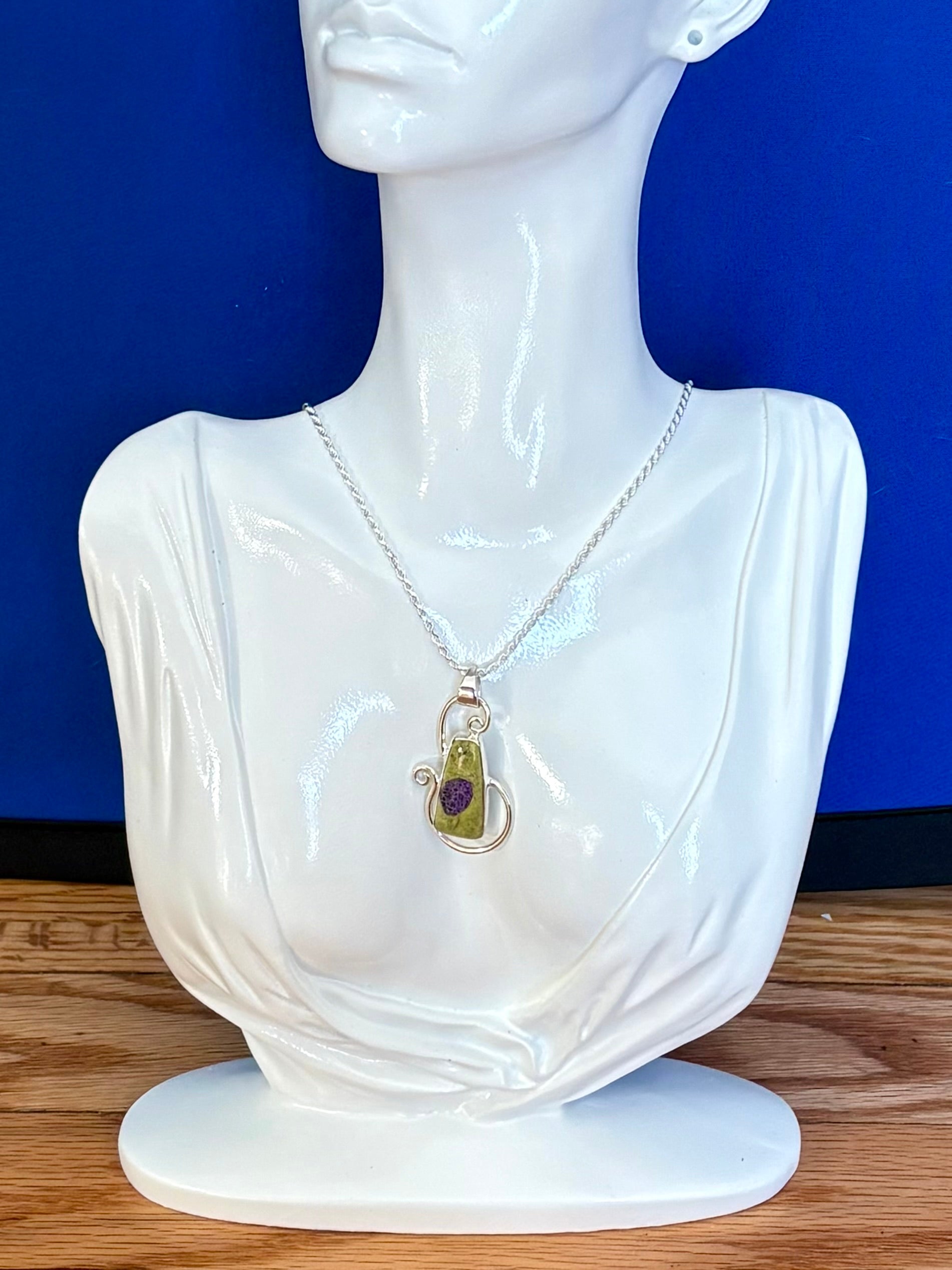Green Alantiste crystal pendant with natural purple inclusion wrapped in silver wire on wooden surface