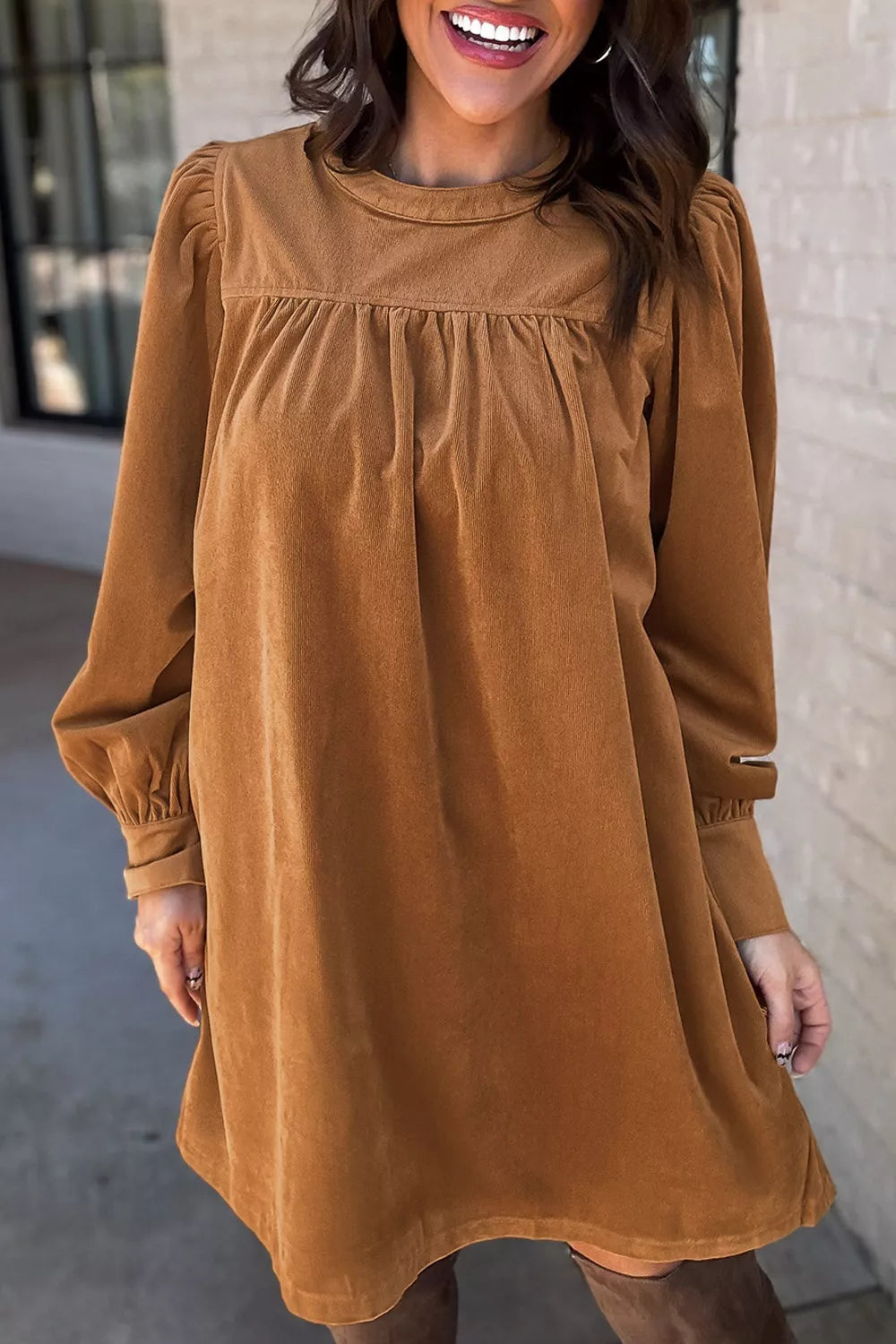 Woman wearing a relaxed long sleeve babydoll dress in warm brown tones with boots