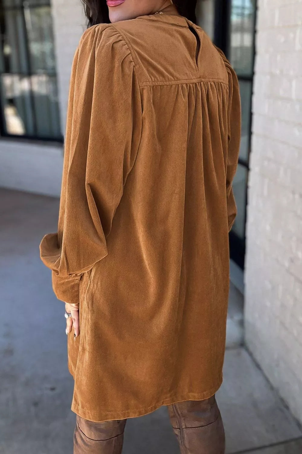 Woman wearing a relaxed long sleeve babydoll dress in warm brown tones with boots