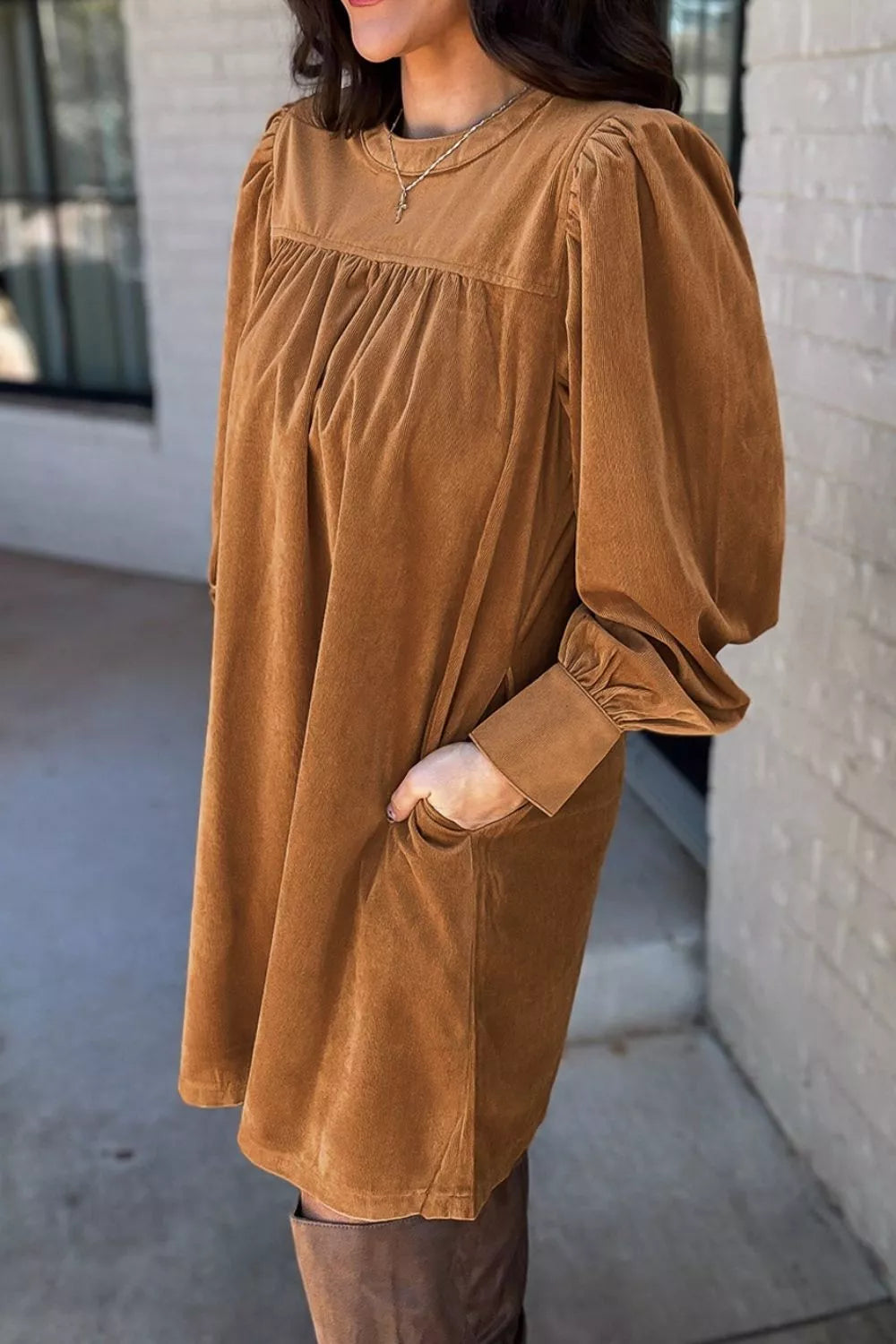 Woman wearing a relaxed long sleeve babydoll dress in warm brown tones with boots