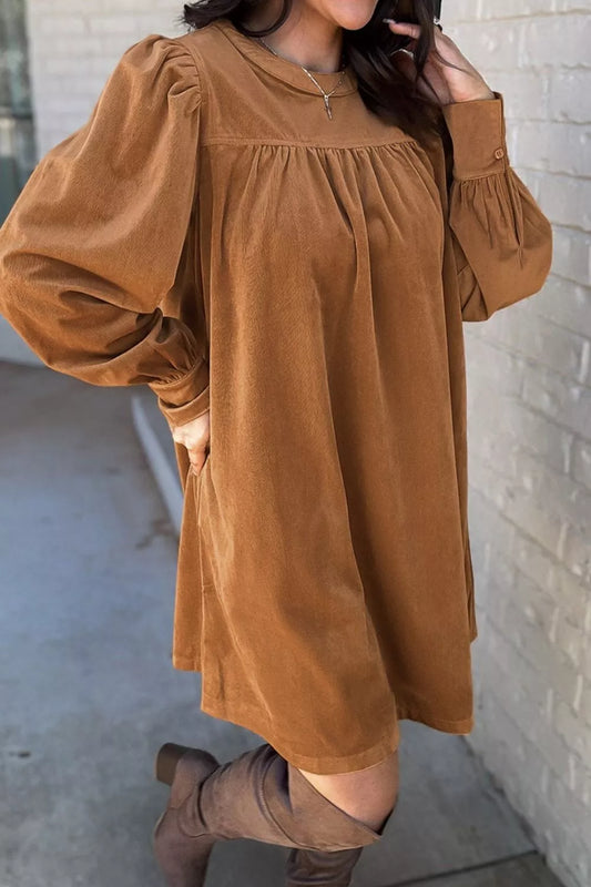 Woman wearing a relaxed long sleeve babydoll dress in warm brown tones with boots