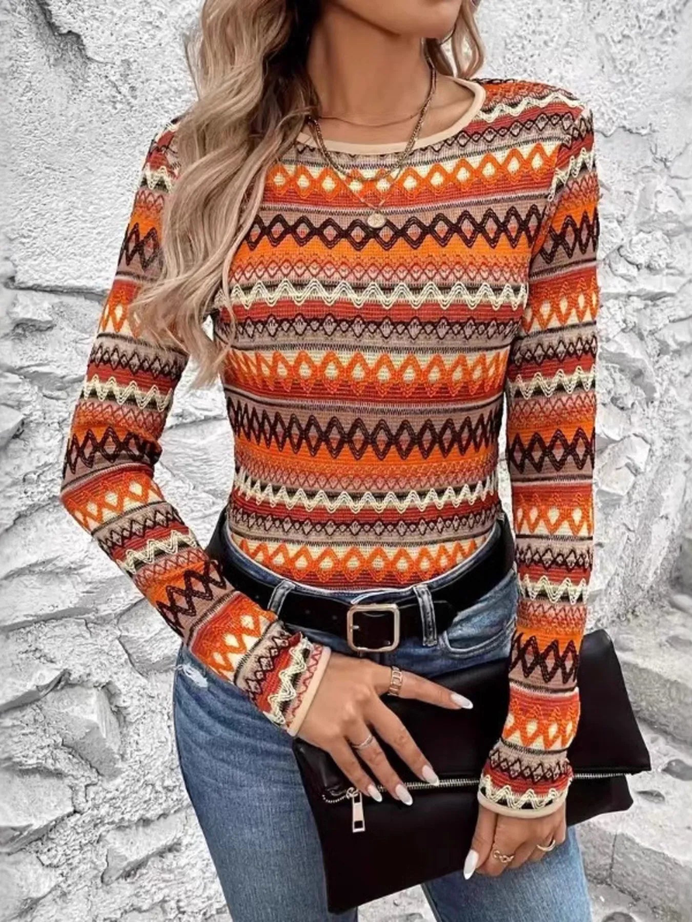 Model wearing Autumn Ember Knit Top with long sleeves and bold geometric knit-style pattern in warm autumn tones of orange, brown, and cream.