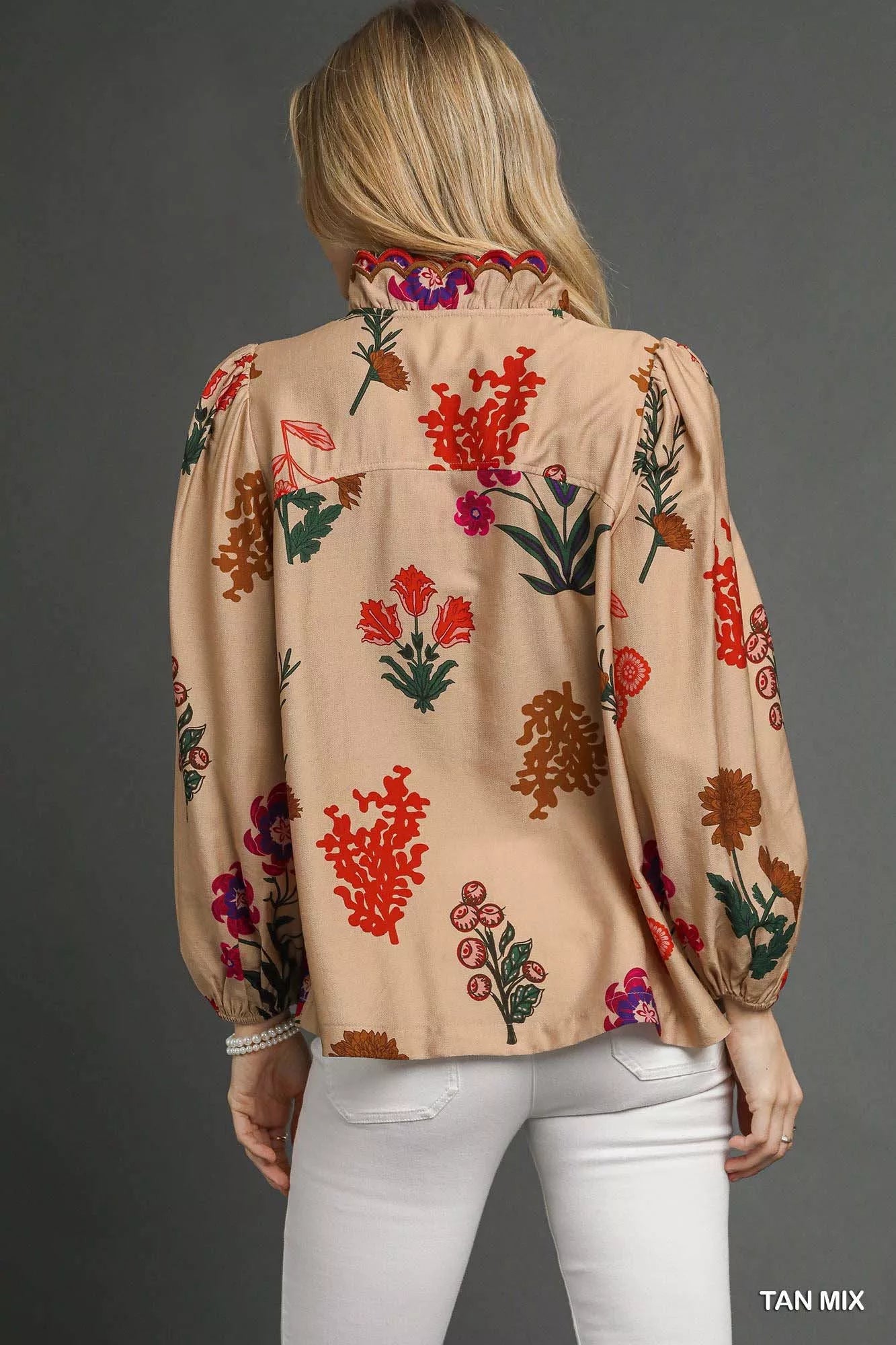Model wearing a beige floral blouse with scalloped red-trim neckline and long puff sleeves, paired with white pants.
