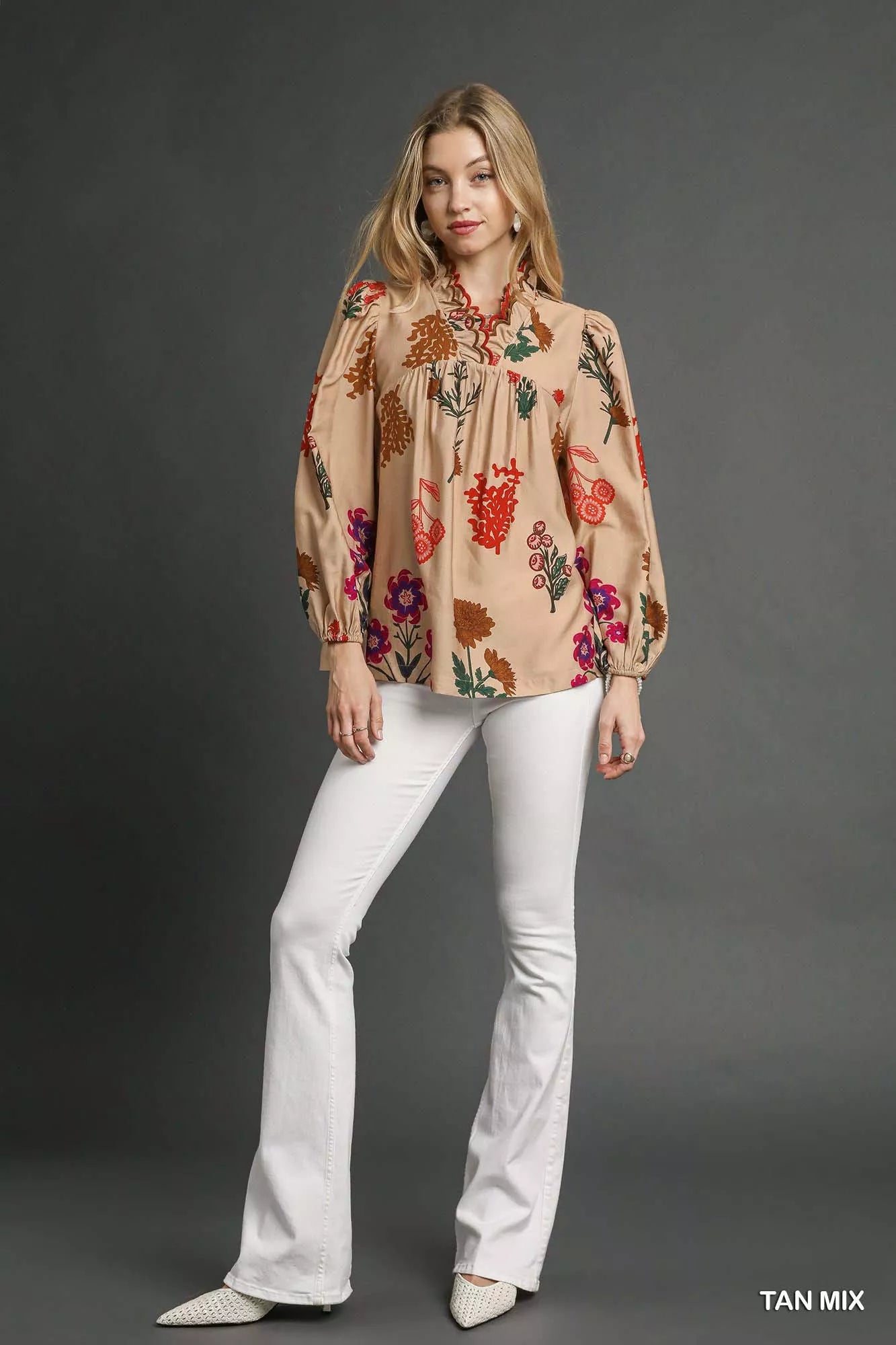 Model wearing a beige floral blouse with scalloped red-trim neckline and long puff sleeves, paired with white pants.