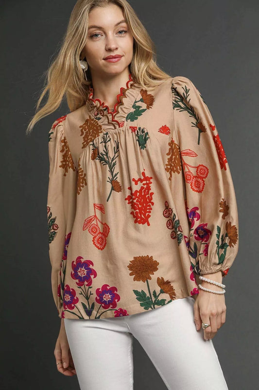 Model wearing a beige floral blouse with scalloped red-trim neckline and long puff sleeves, paired with white pants.