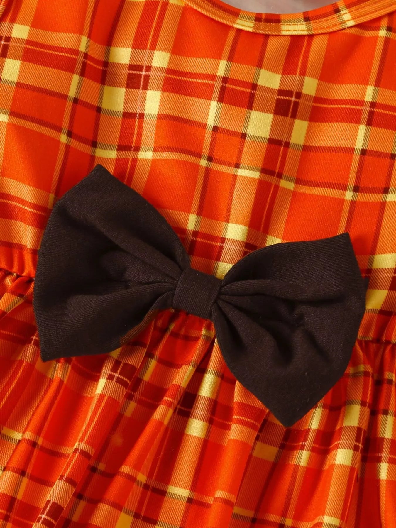 Three-piece baby girl outfit with orange plaid turkey dress, brown cardigan, and matching plaid headband on a beige background with fall leaves.