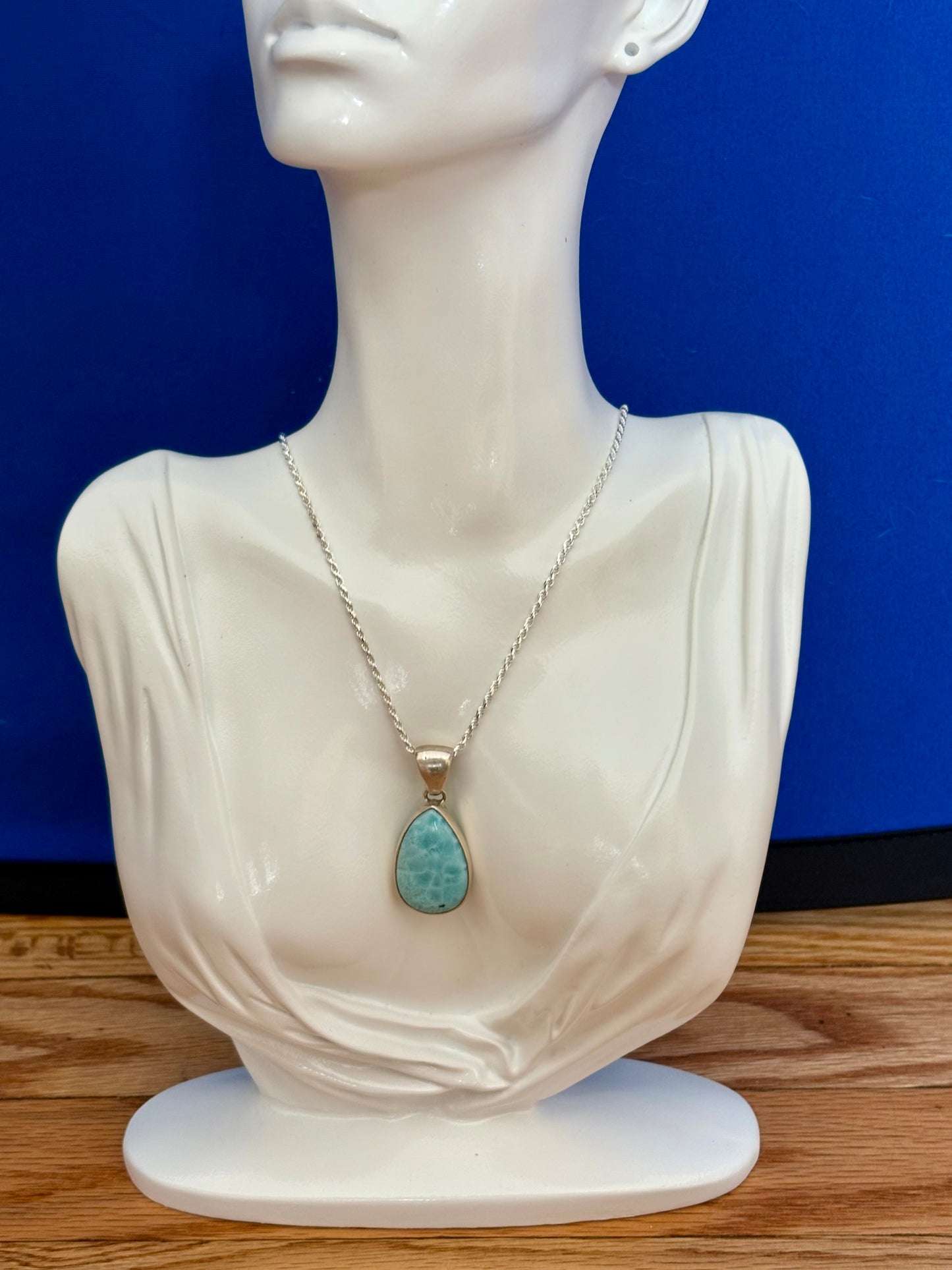 Teardrop-shaped blue larimar gemstone pendant with natural marbling on a neutral stone background