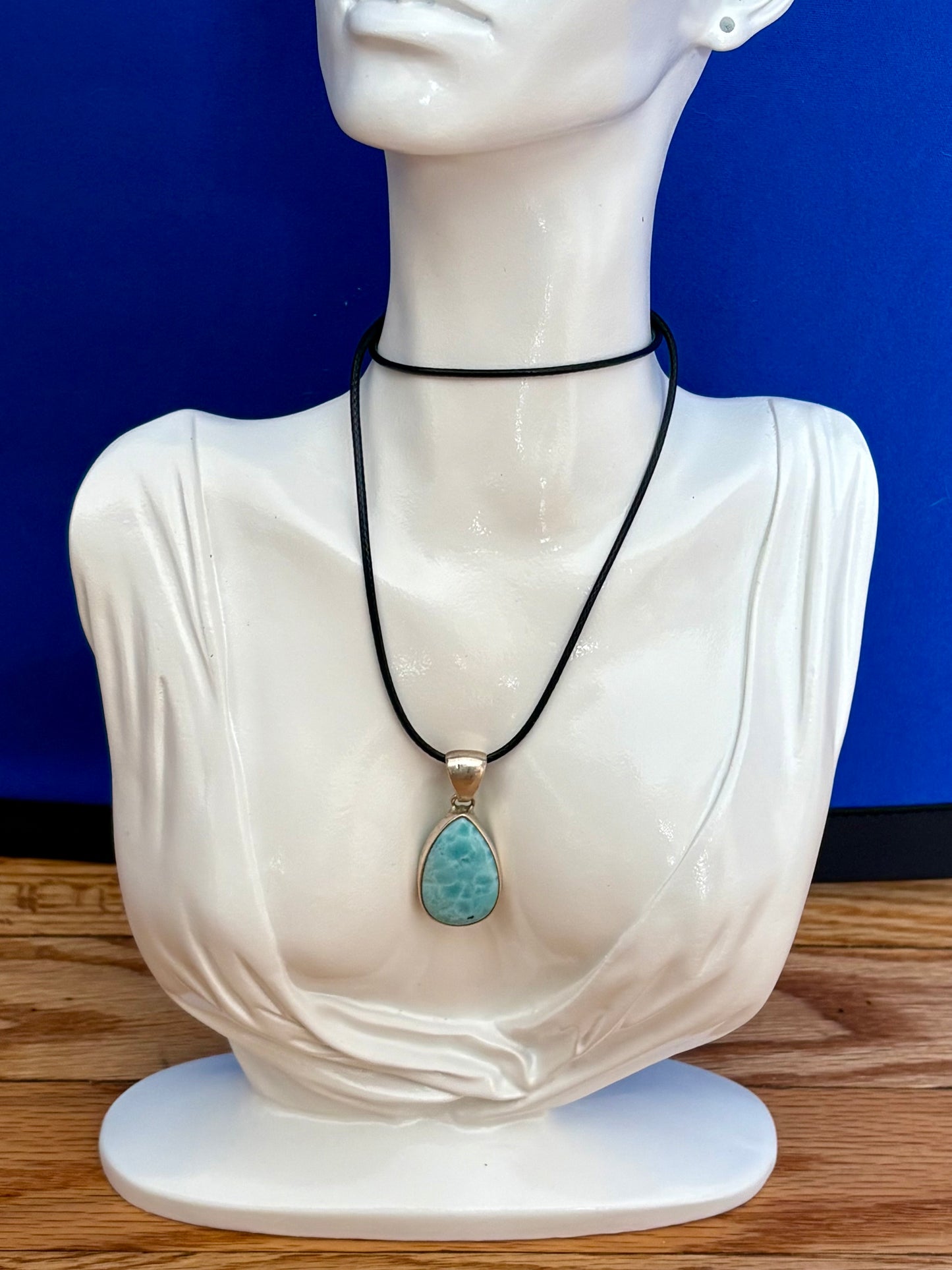 Teardrop-shaped blue larimar gemstone pendant with natural marbling on a neutral stone background