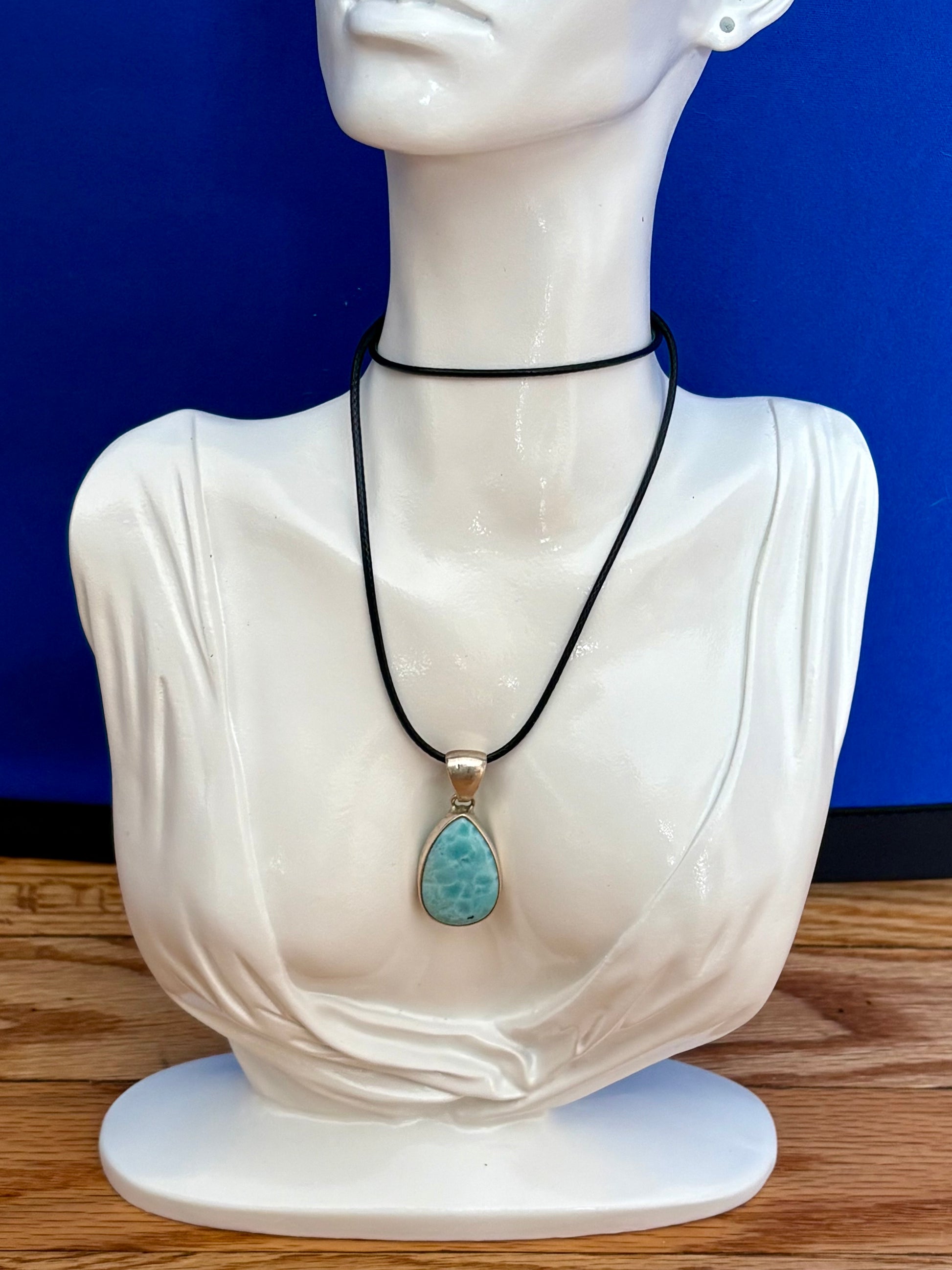 Teardrop-shaped blue larimar gemstone pendant with natural marbling on a neutral stone background