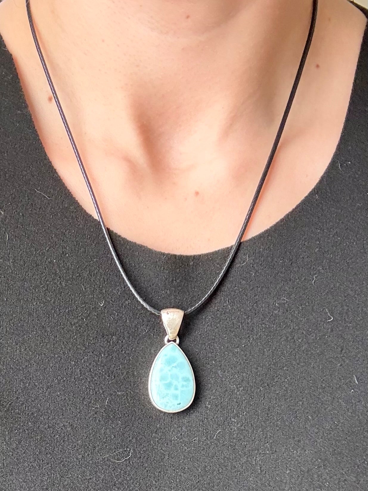 Teardrop-shaped blue larimar gemstone pendant with natural marbling on a neutral stone background