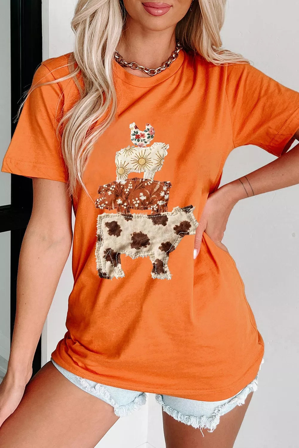 Orange short sleeve graphic tee with stacked patchwork-style farm animals including a cow, pig, sheep, and chicken.