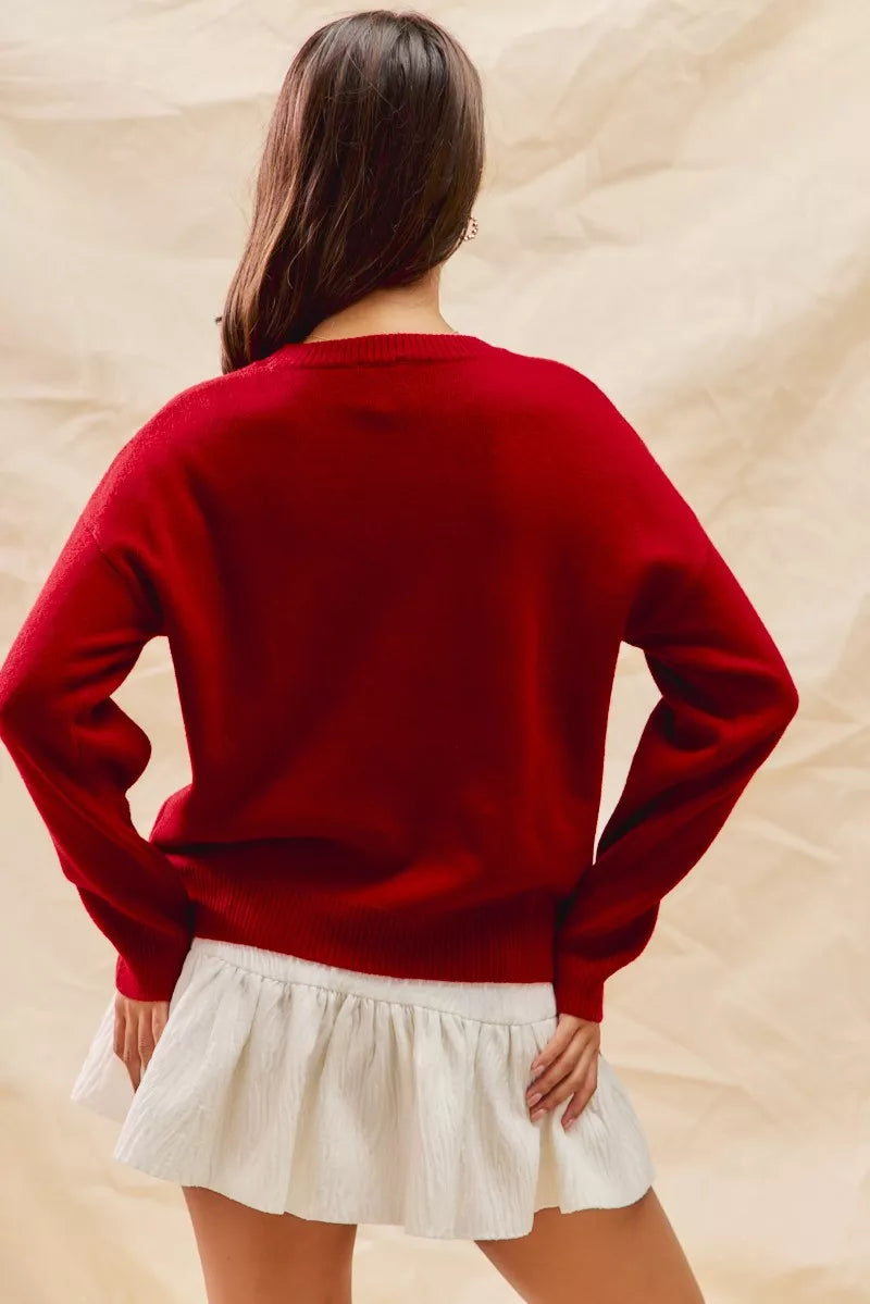Woman wearing a red Christmas sweater with an appliqué teddy bear and plaid bow detail — cozy festive knit from A Whimsical Affair.