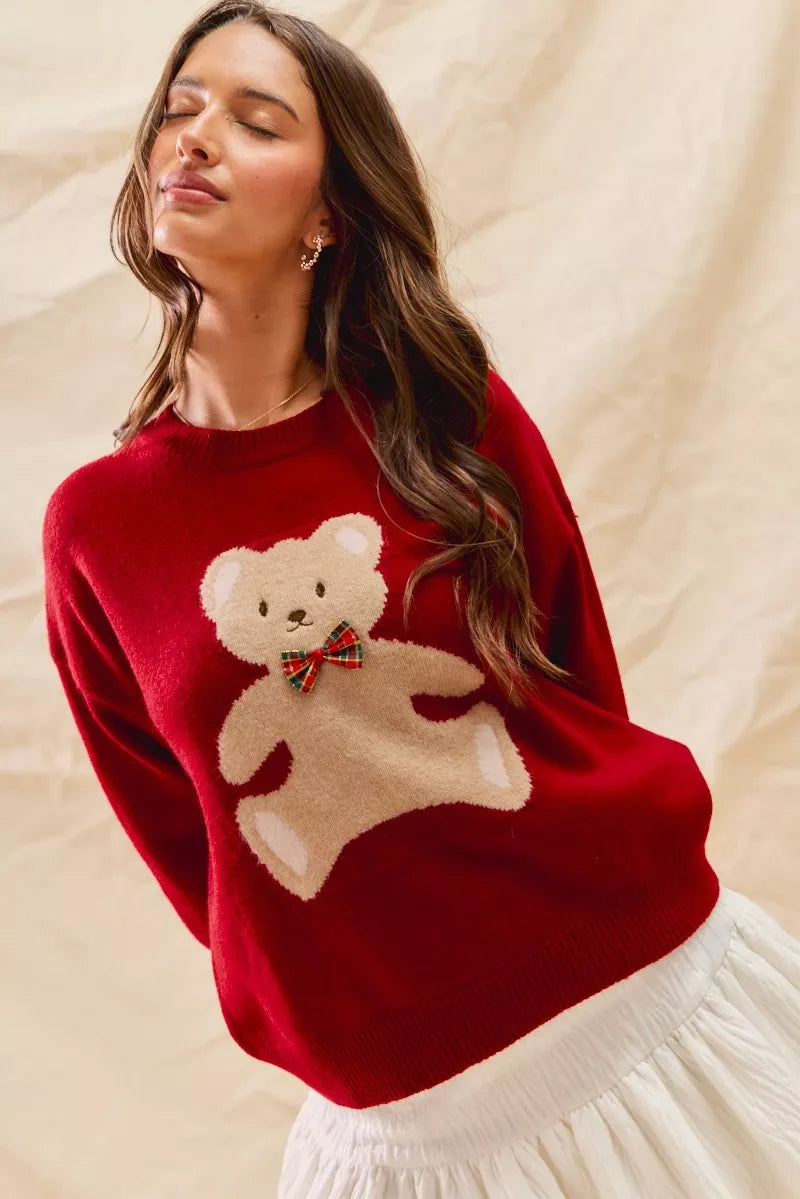 Woman wearing a red Christmas sweater with an appliqué teddy bear and plaid bow detail — cozy festive knit from A Whimsical Affair.