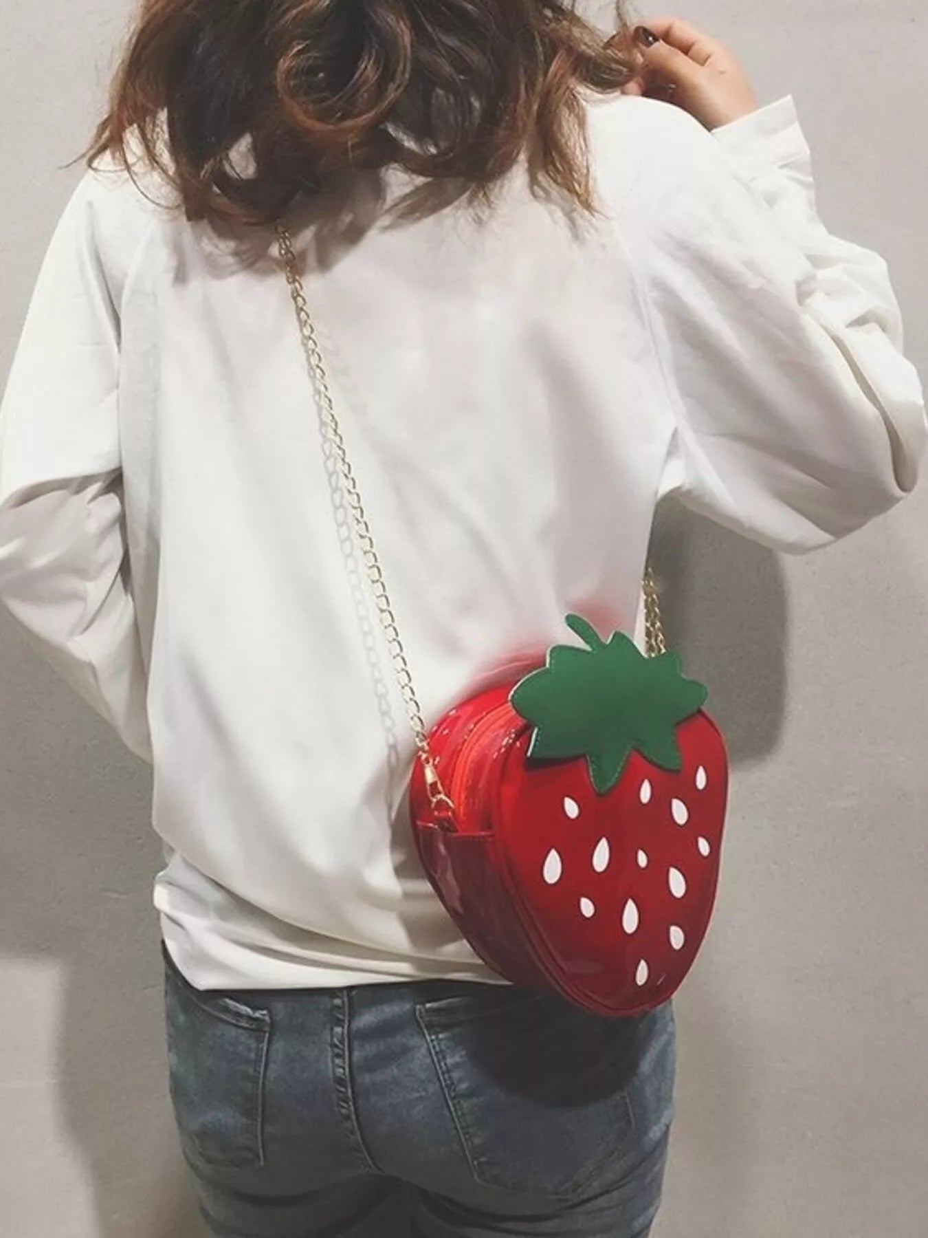 Glossy red strawberry-shaped mini bag with green leaf top and gold chain strap, displayed on a neutral background for a cute and playful look.