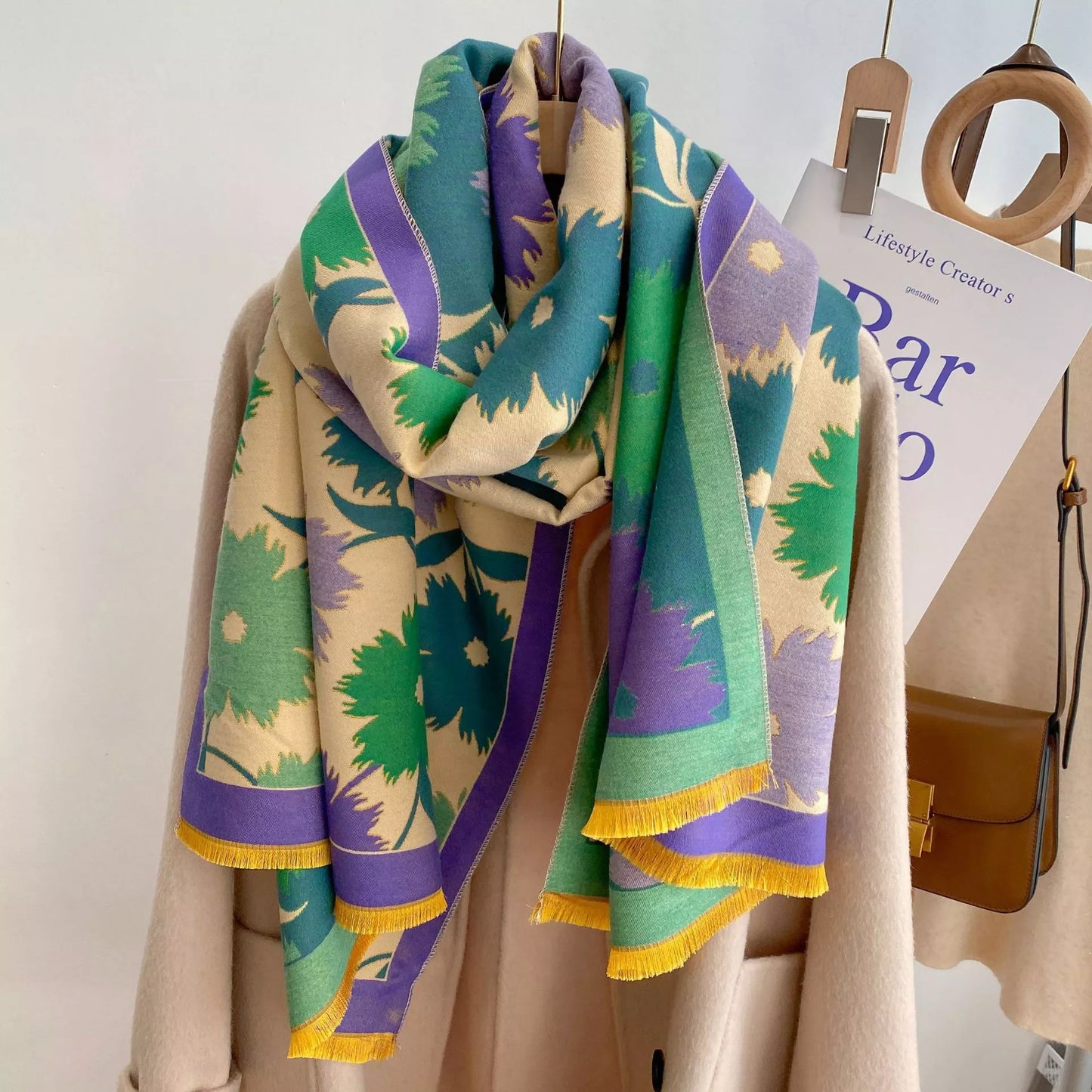 Oversized floral fringe scarf draped over a coat, featuring soft multicolor botanical patterns and lightweight fabric