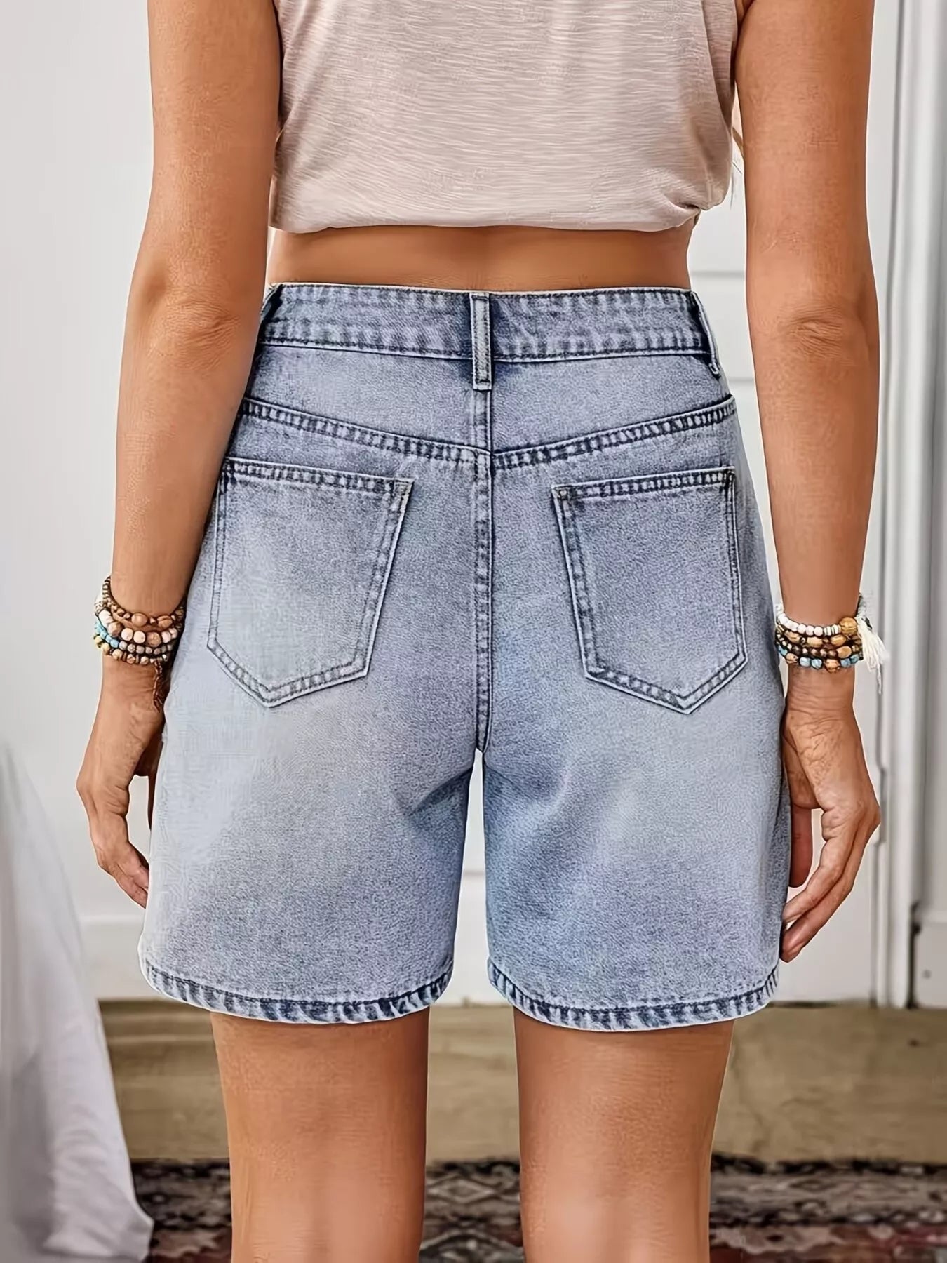 Light wash denim shorts with floral embroidery, appliqué details, button closure, pockets, and structured cotton-blend fabric.