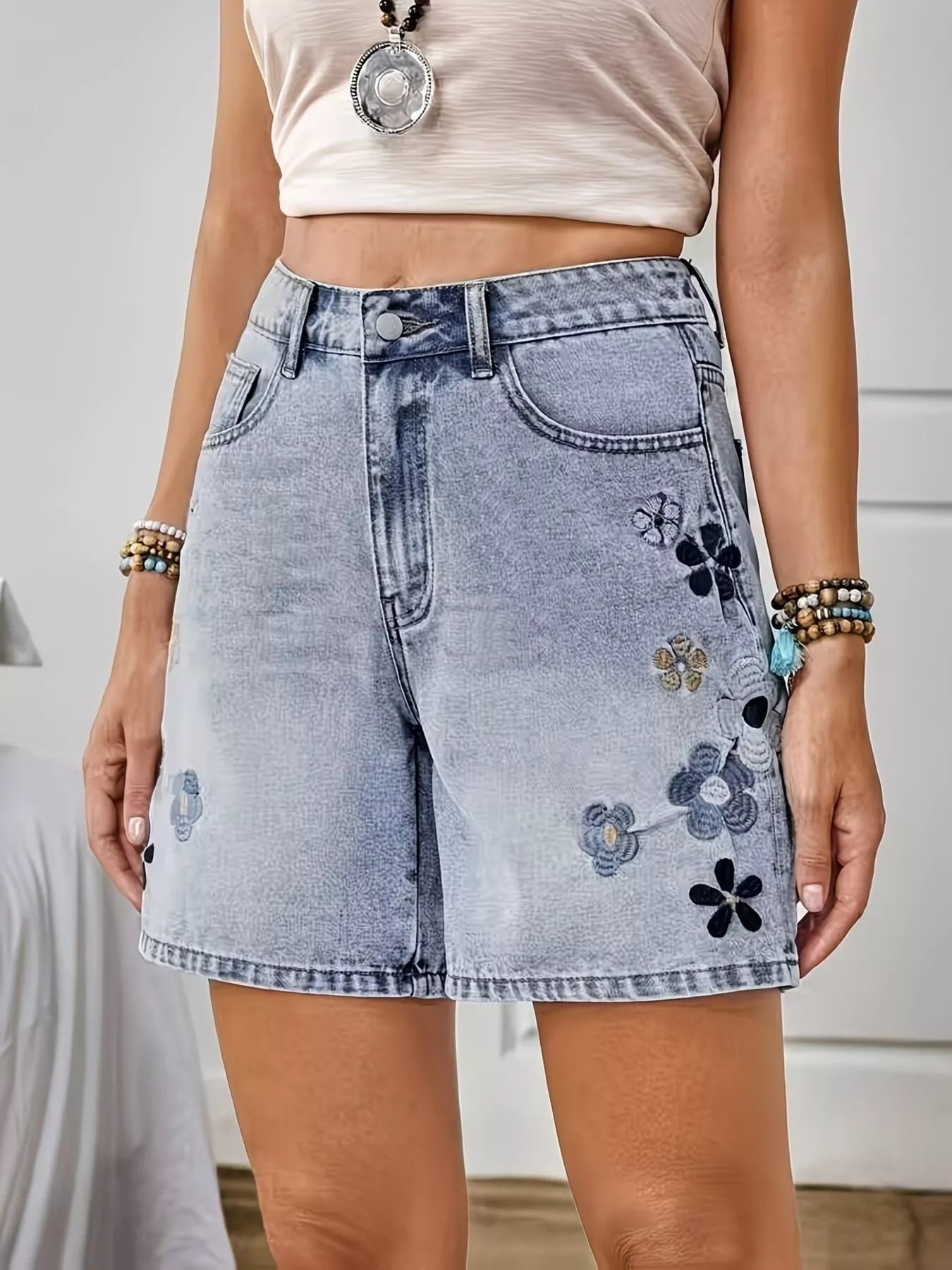 Light wash denim shorts with floral embroidery, appliqué details, button closure, pockets, and structured cotton-blend fabric.