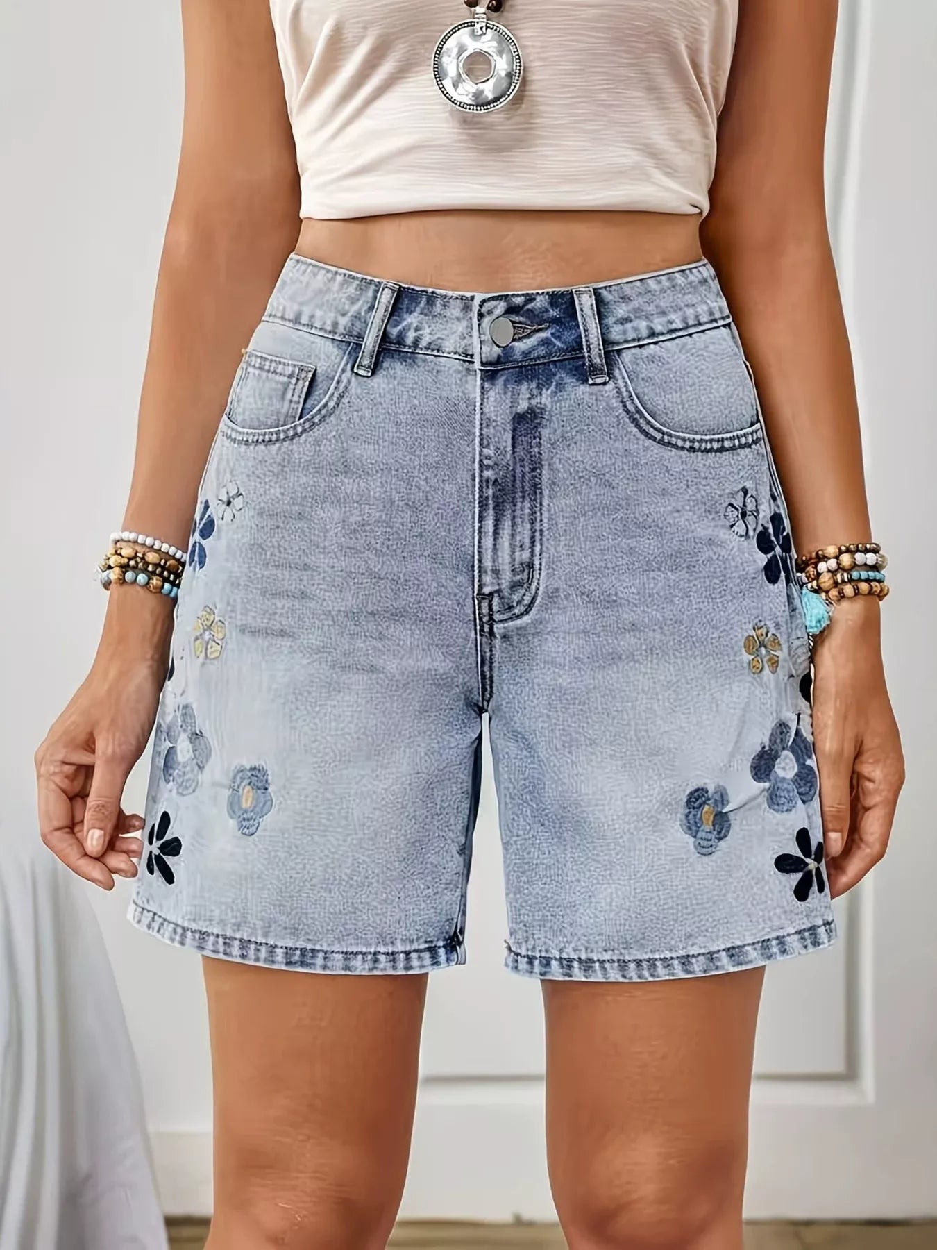 Light wash denim shorts with floral embroidery, appliqué details, button closure, pockets, and structured cotton-blend fabric.