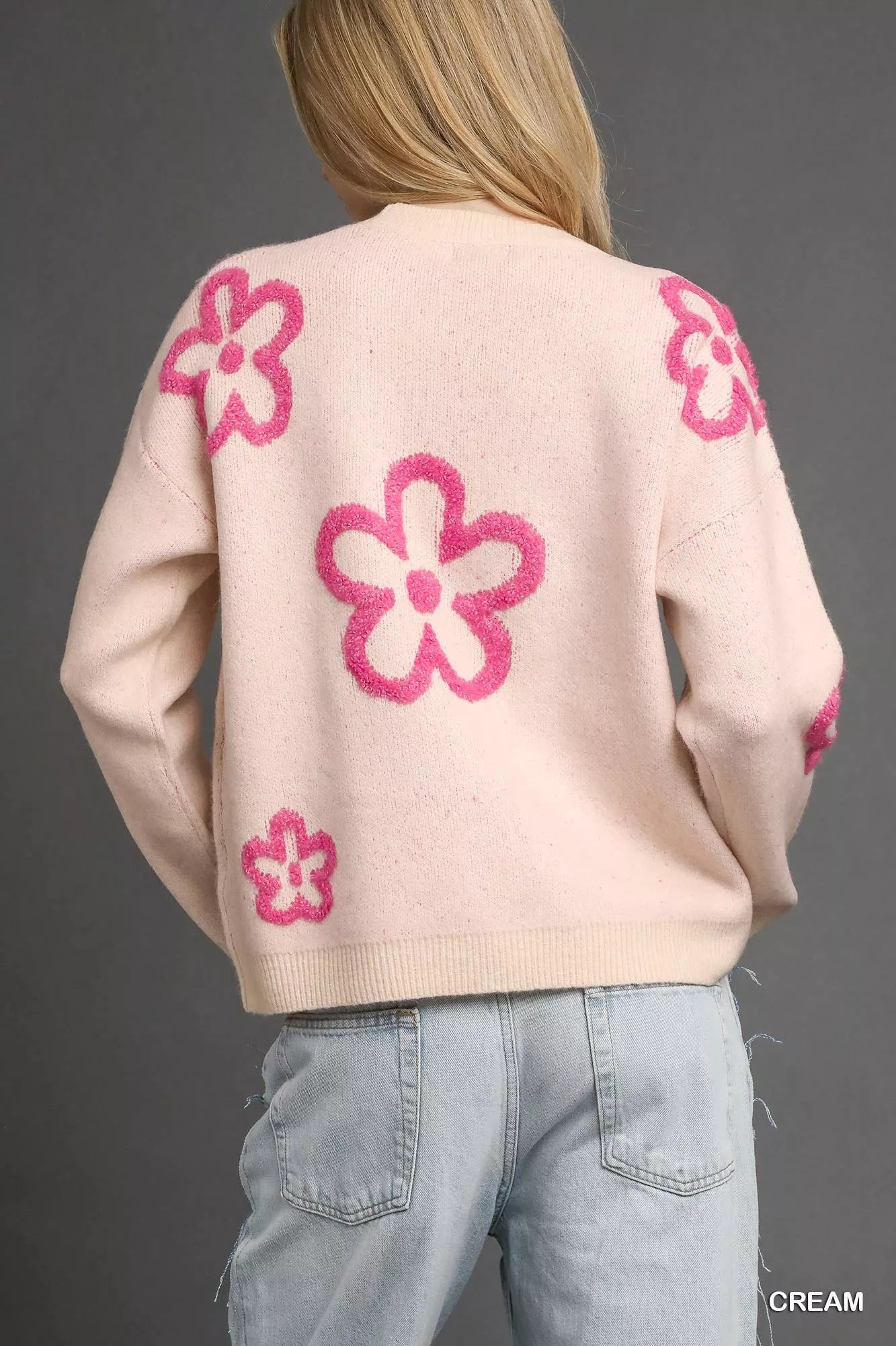 Woman wearing a cream sweater with bold pink floral accents and a round neckline.