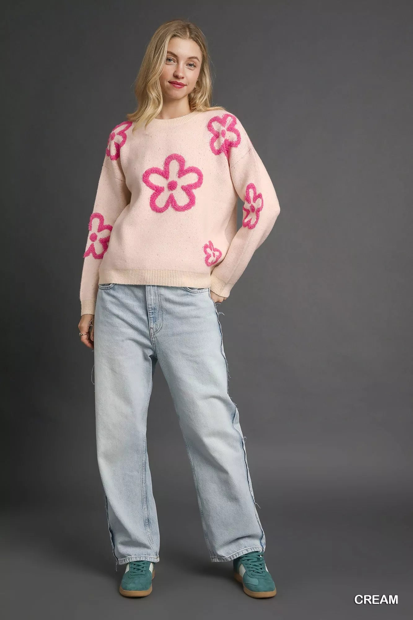Woman wearing a cream sweater with bold pink floral accents and a round neckline.