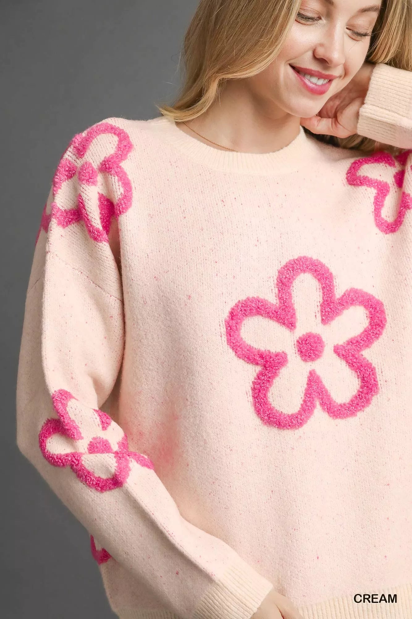 Woman wearing a cream sweater with bold pink floral accents and a round neckline.