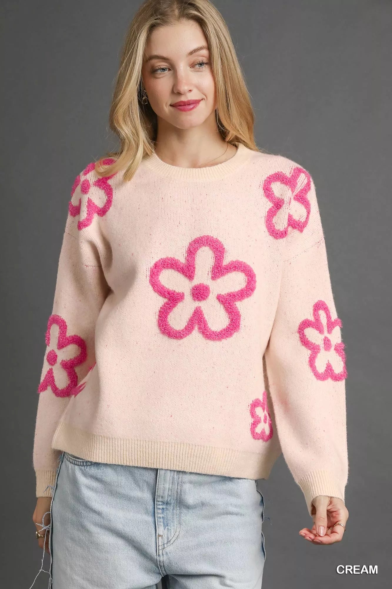 Woman wearing a cream sweater with bold pink floral accents and a round neckline.