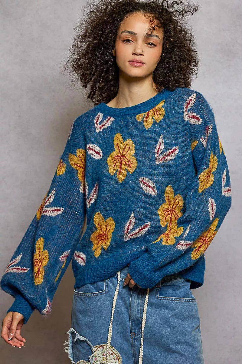 Model wearing the Blue Dusk Bloom Sweater — a blue mohair-blend knit with yellow floral patterns and balloon sleeves, styled with relaxed denim.