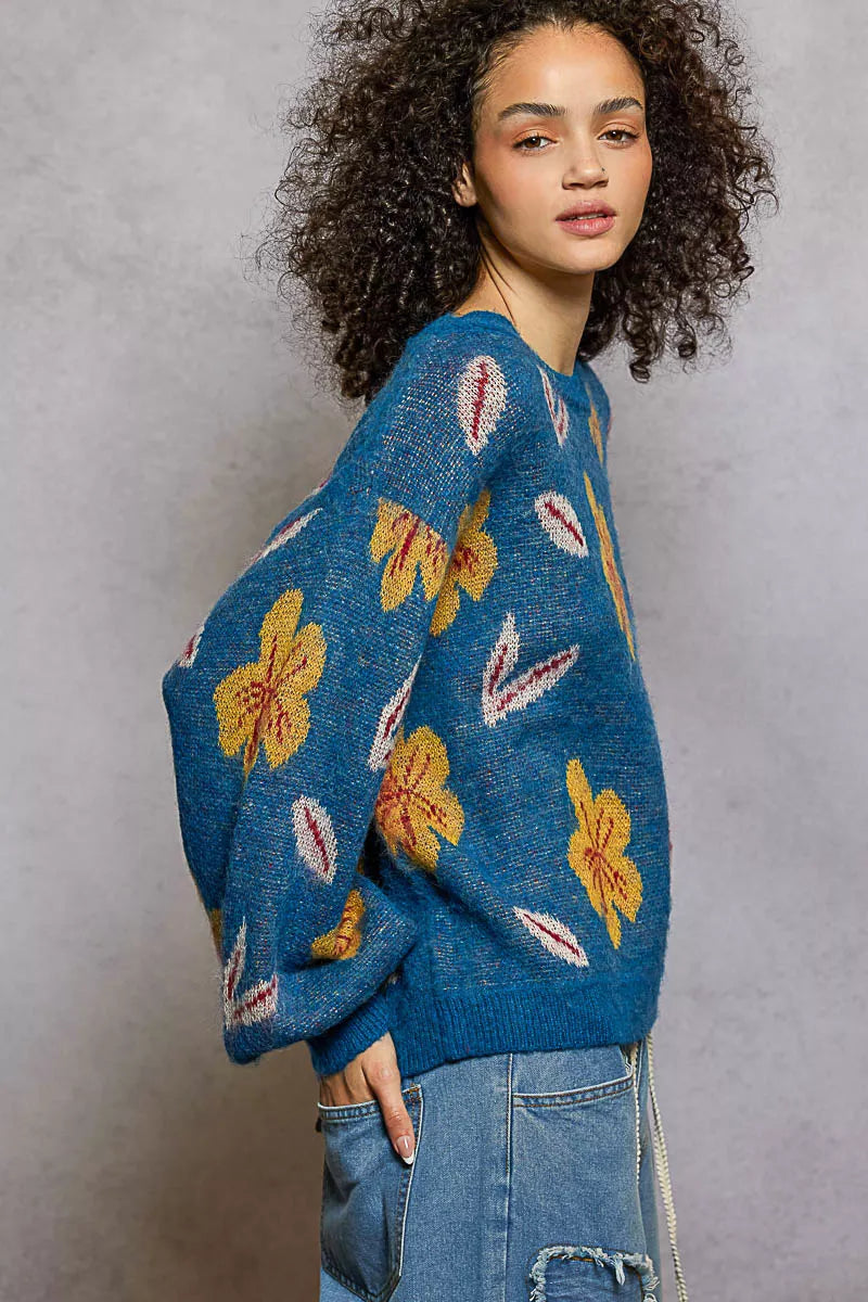 Model wearing the Blue Dusk Bloom Sweater — a blue mohair-blend knit with yellow floral patterns and balloon sleeves, styled with relaxed denim.