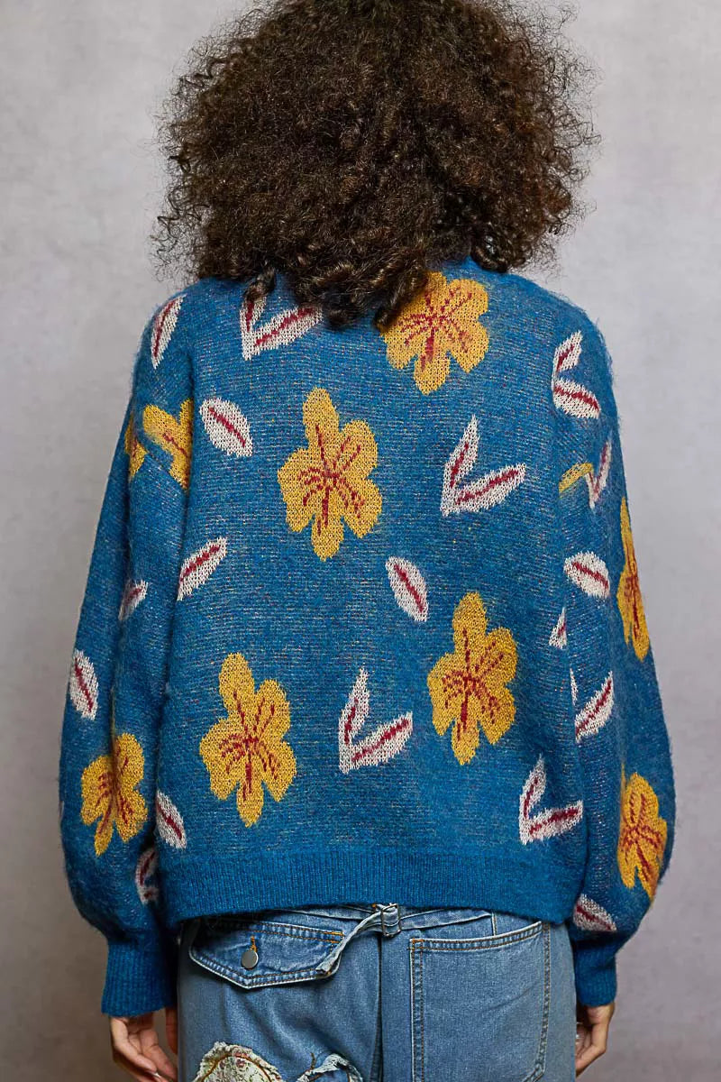 Model wearing the Blue Dusk Bloom Sweater — a blue mohair-blend knit with yellow floral patterns and balloon sleeves, styled with relaxed denim.
