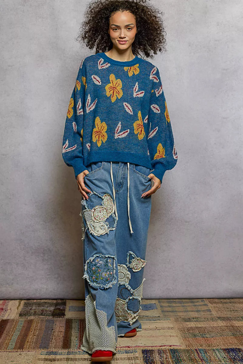 Model wearing the Blue Dusk Bloom Sweater — a blue mohair-blend knit with yellow floral patterns and balloon sleeves, styled with relaxed denim.