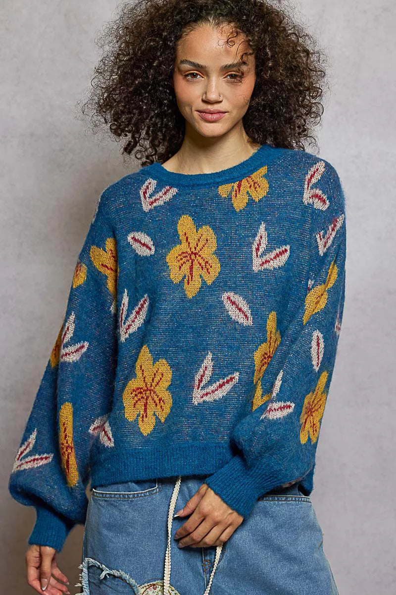 Model wearing the Blue Dusk Bloom Sweater — a blue mohair-blend knit with yellow floral patterns and balloon sleeves, styled with relaxed denim.