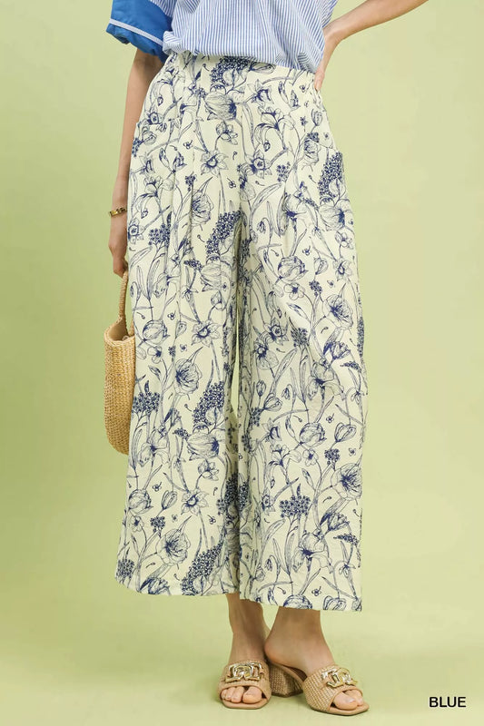 Wide-leg pants with blue botanical floral print, pleated design, elastic waistband, and relaxed fit on a light background