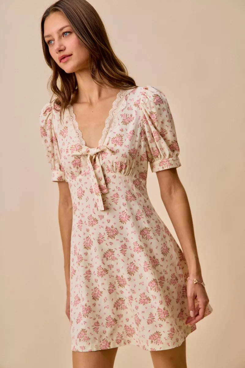 Cream floral mini dress with lace-trim neckline, front bow detail, short sleeves, and romantic vintage-inspired print