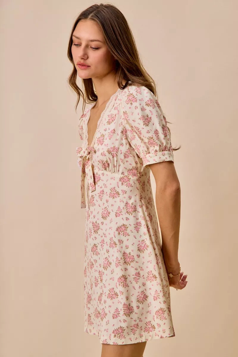 Cream floral mini dress with lace-trim neckline, front bow detail, short sleeves, and romantic vintage-inspired print