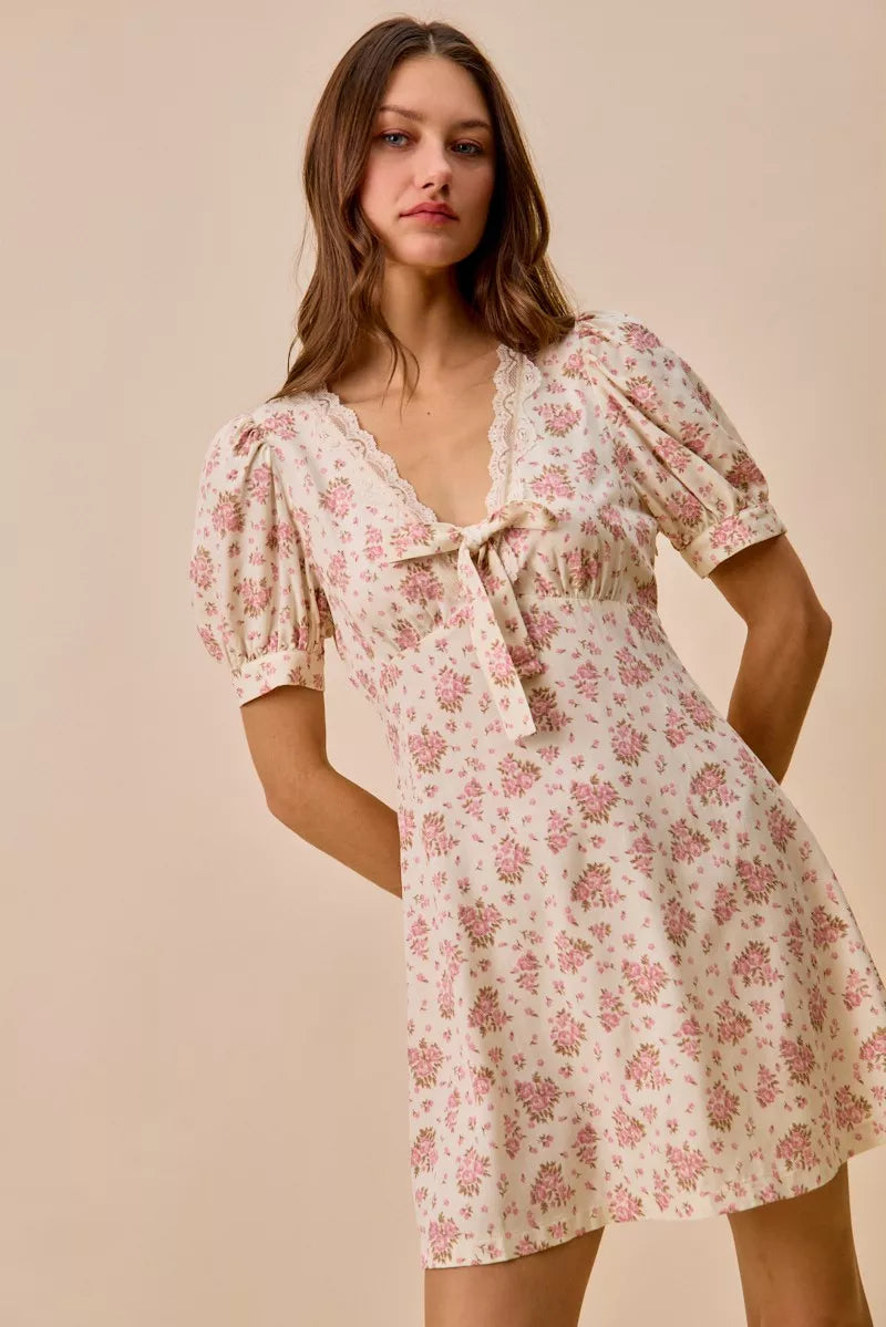 Cream floral mini dress with lace-trim neckline, front bow detail, short sleeves, and romantic vintage-inspired print