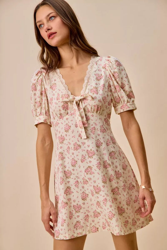 Cream floral mini dress with lace-trim neckline, front bow detail, short sleeves, and romantic vintage-inspired print